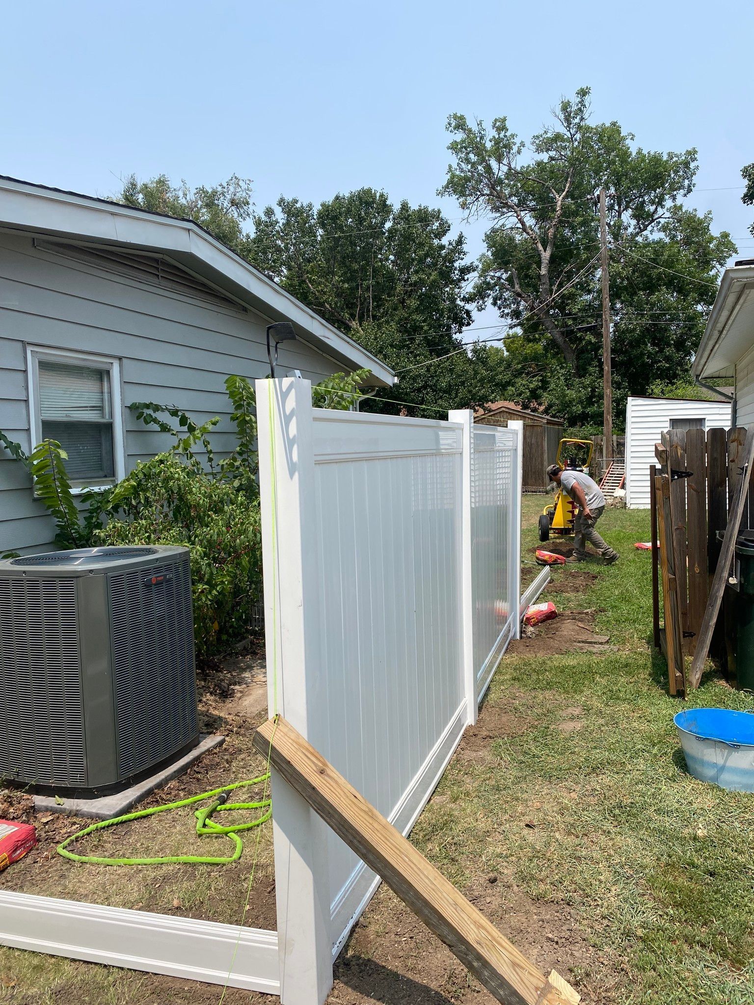 White vinyl fence being installed between two houses; a worker can be seen.