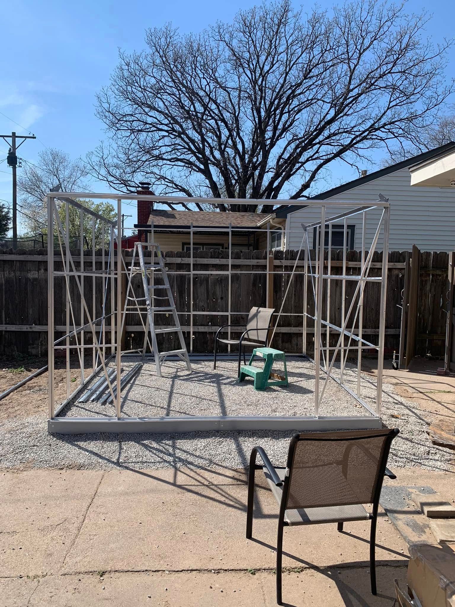 Metal frame structure being built in a backyard, with a chair in the foreground.