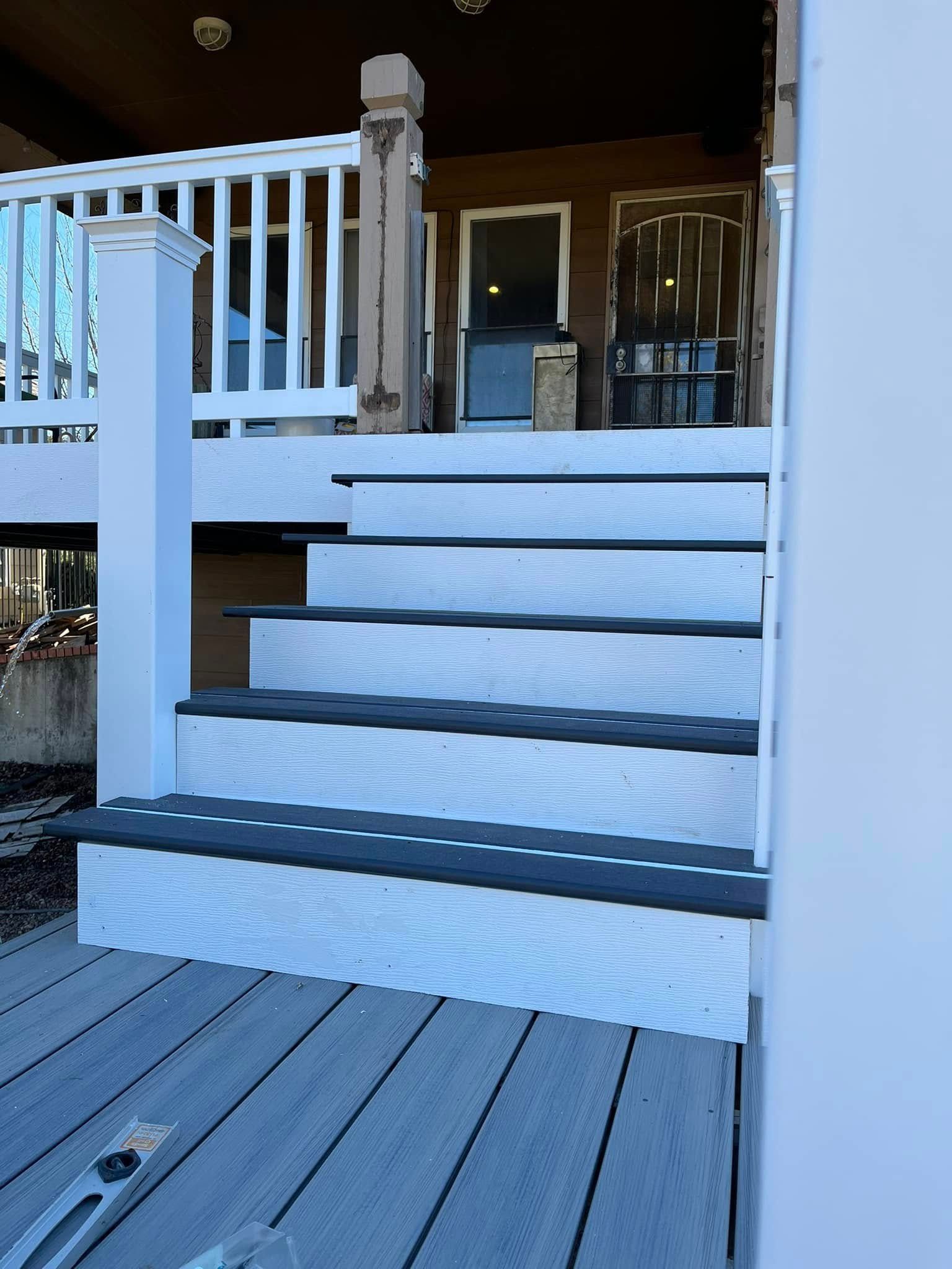 Staircase with gray and black composite steps leading up to a deck and house entrance.