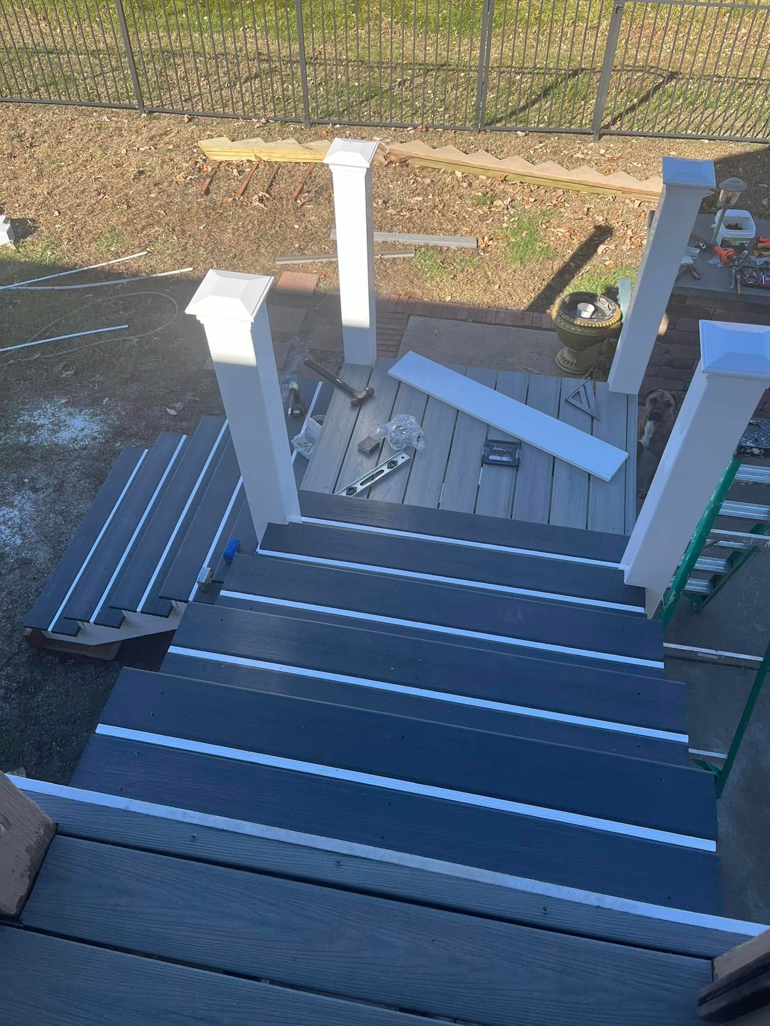 Deck with stairs under construction; gray composite decking, white columns, outdoor setting.