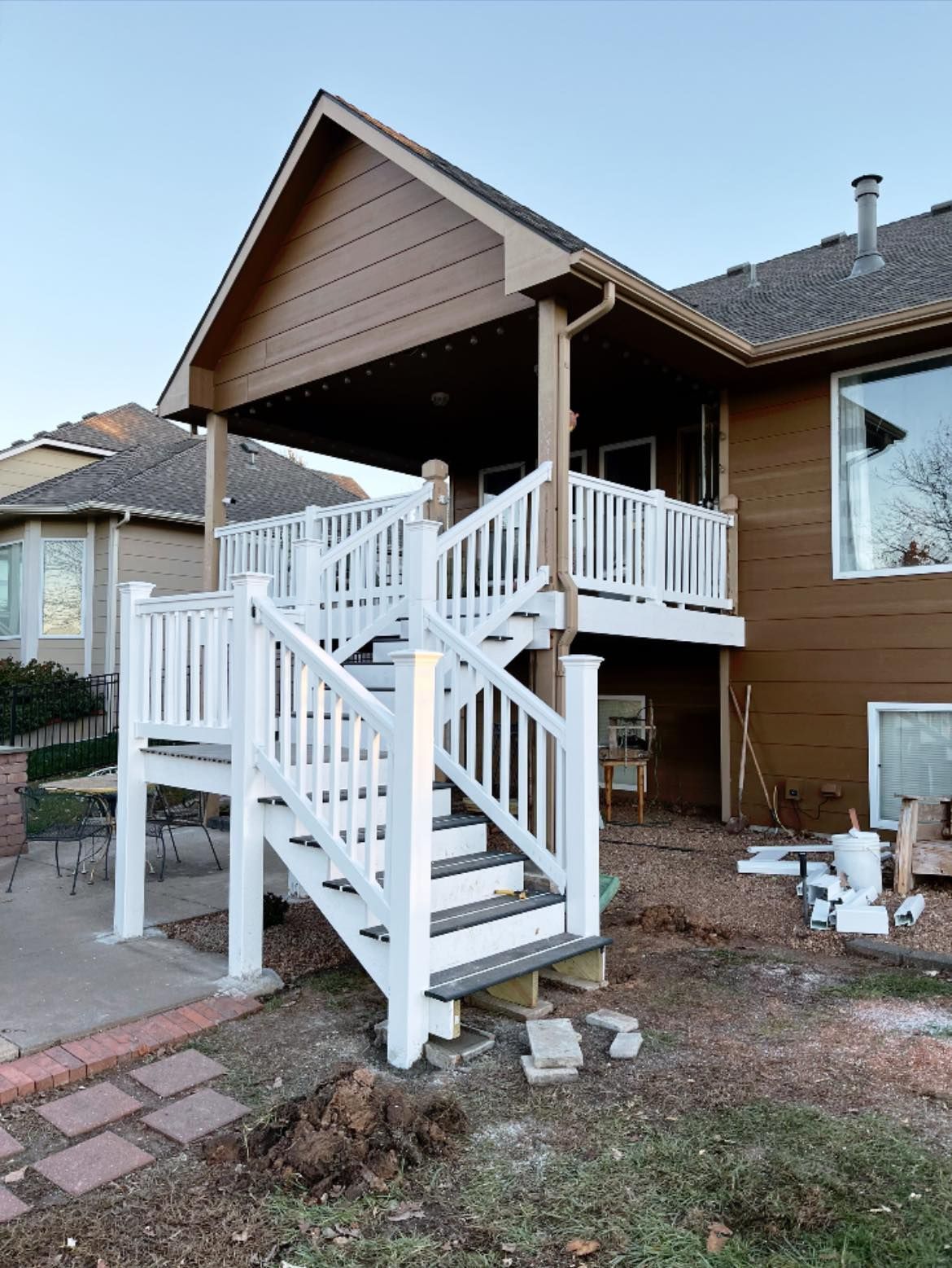 White deck with stairs attached to a brown house with a covered patio.