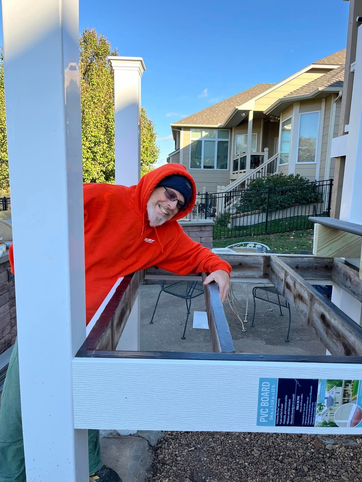 Man in orange hoodie smiling, building structure outside. Blue sky, residential background.