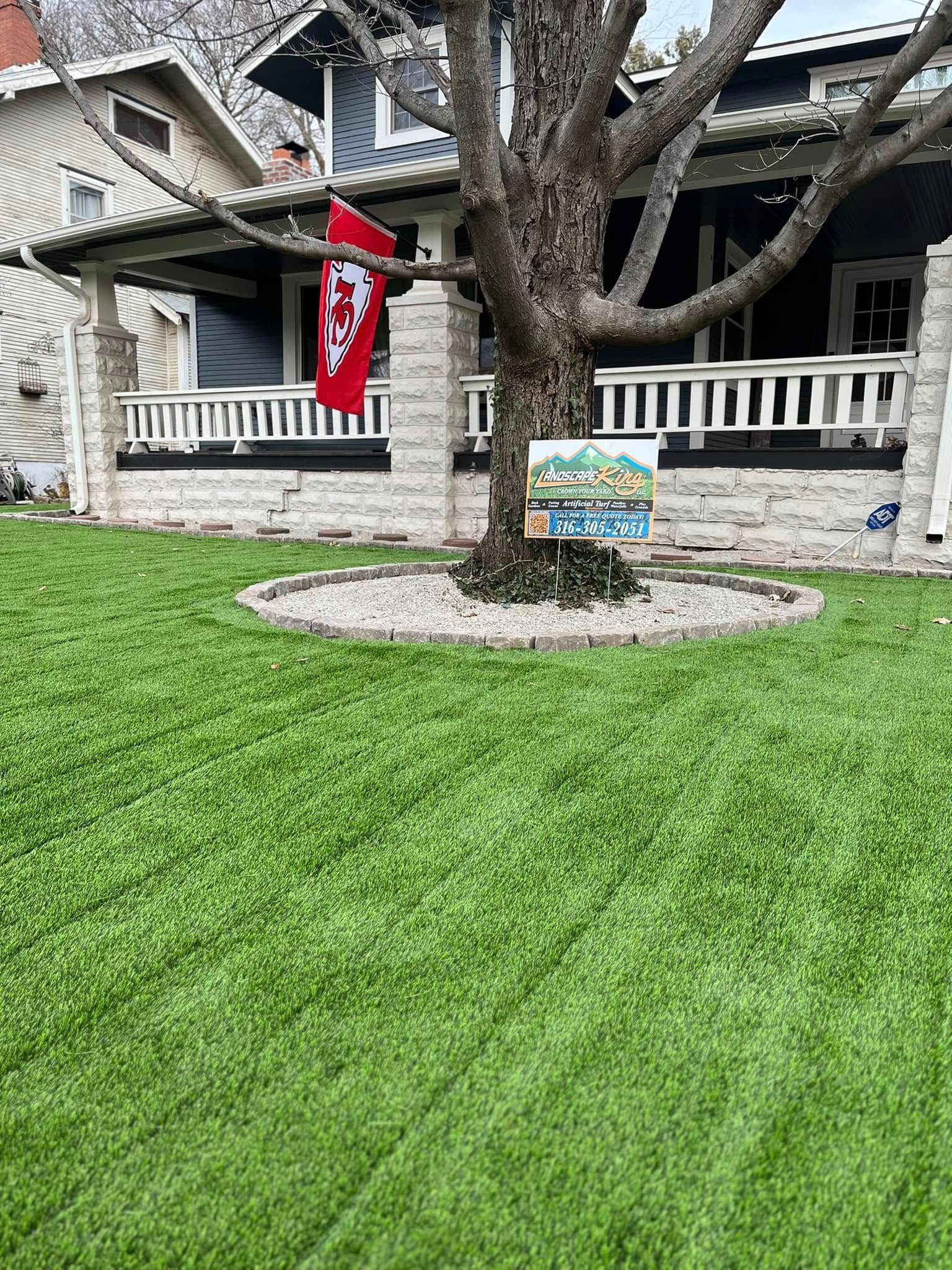 A house with a flag, tree with a sign, and green lawn in front.