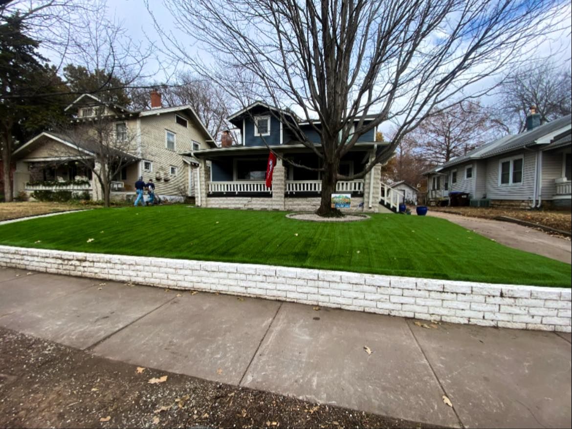 A two-story house with lush green lawn behind a white brick wall, street view.