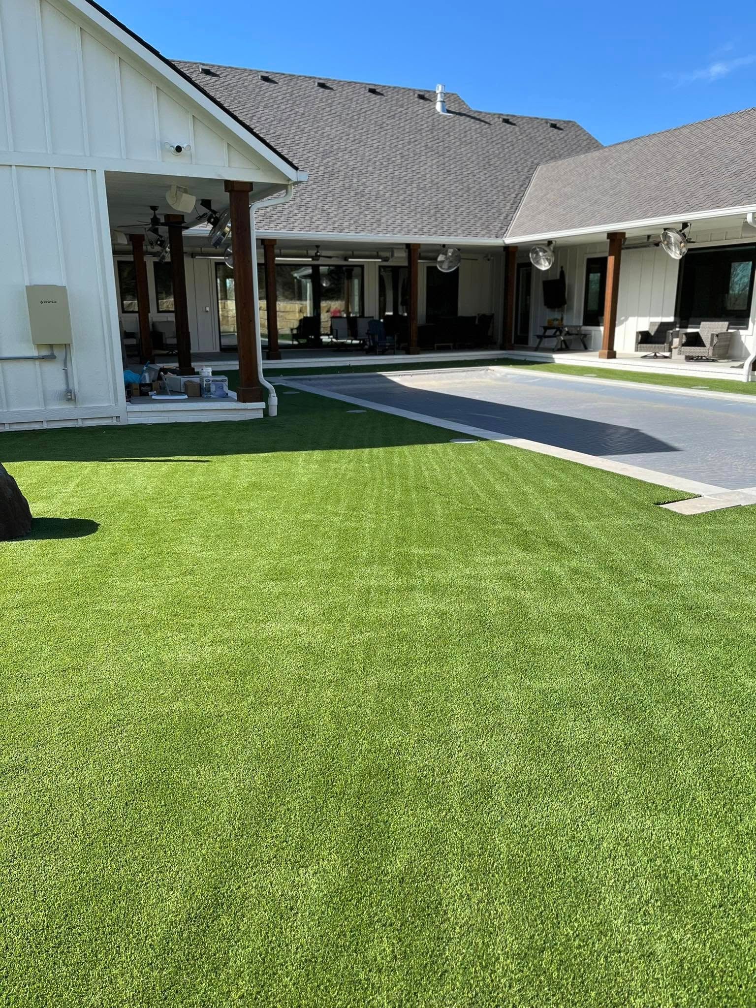 A bright green lawn with a white house and dark roof.