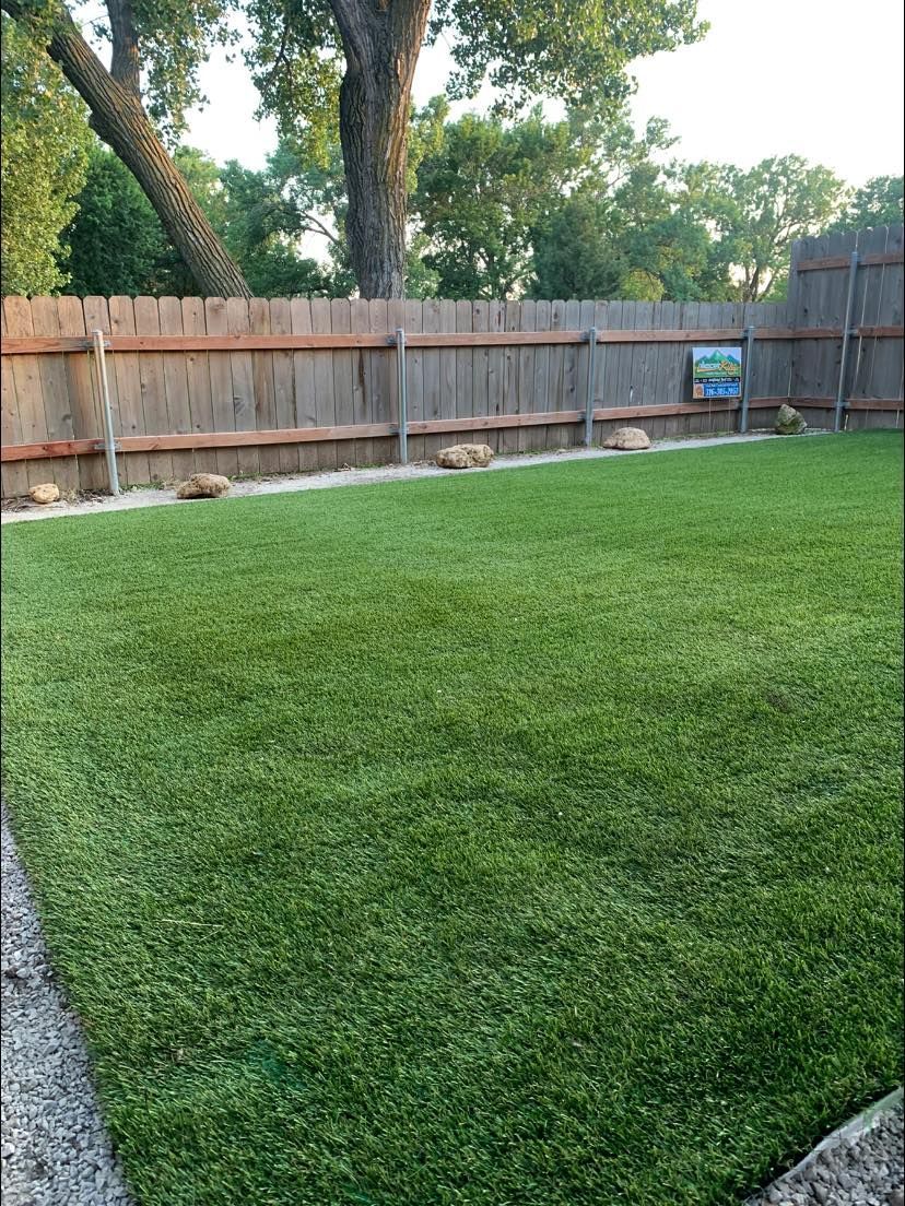Green, well-kept artificial grass backyard bordered by a wooden fence and gravel.