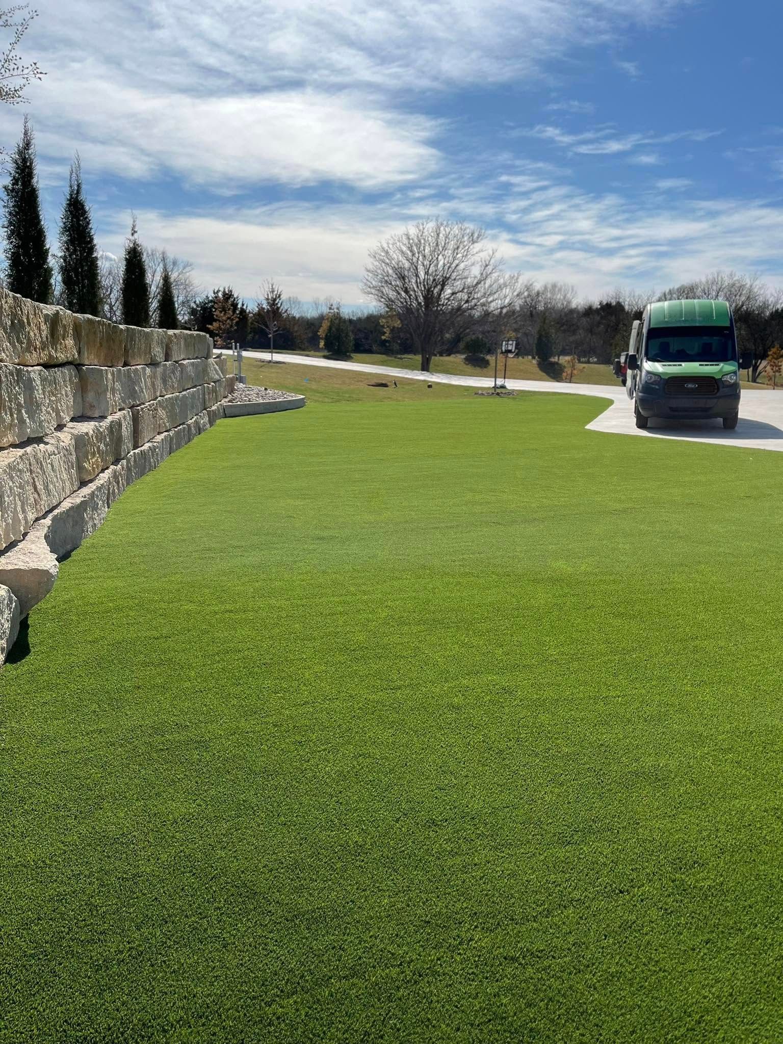 Green grass yard with a stone wall, tree, blue sky, and a green van.