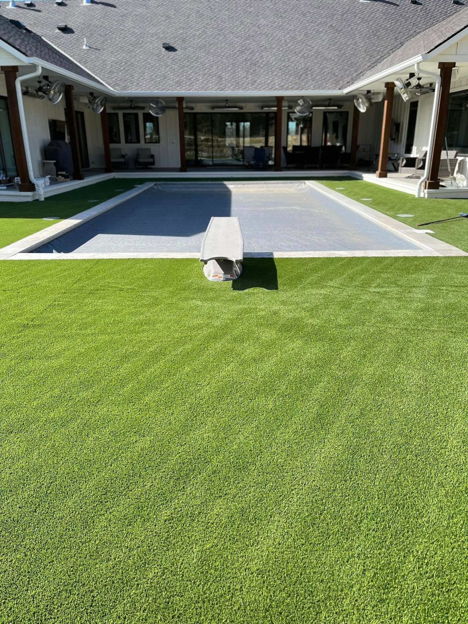Backyard with a pool and green turf, surrounded by a house with a covered patio.