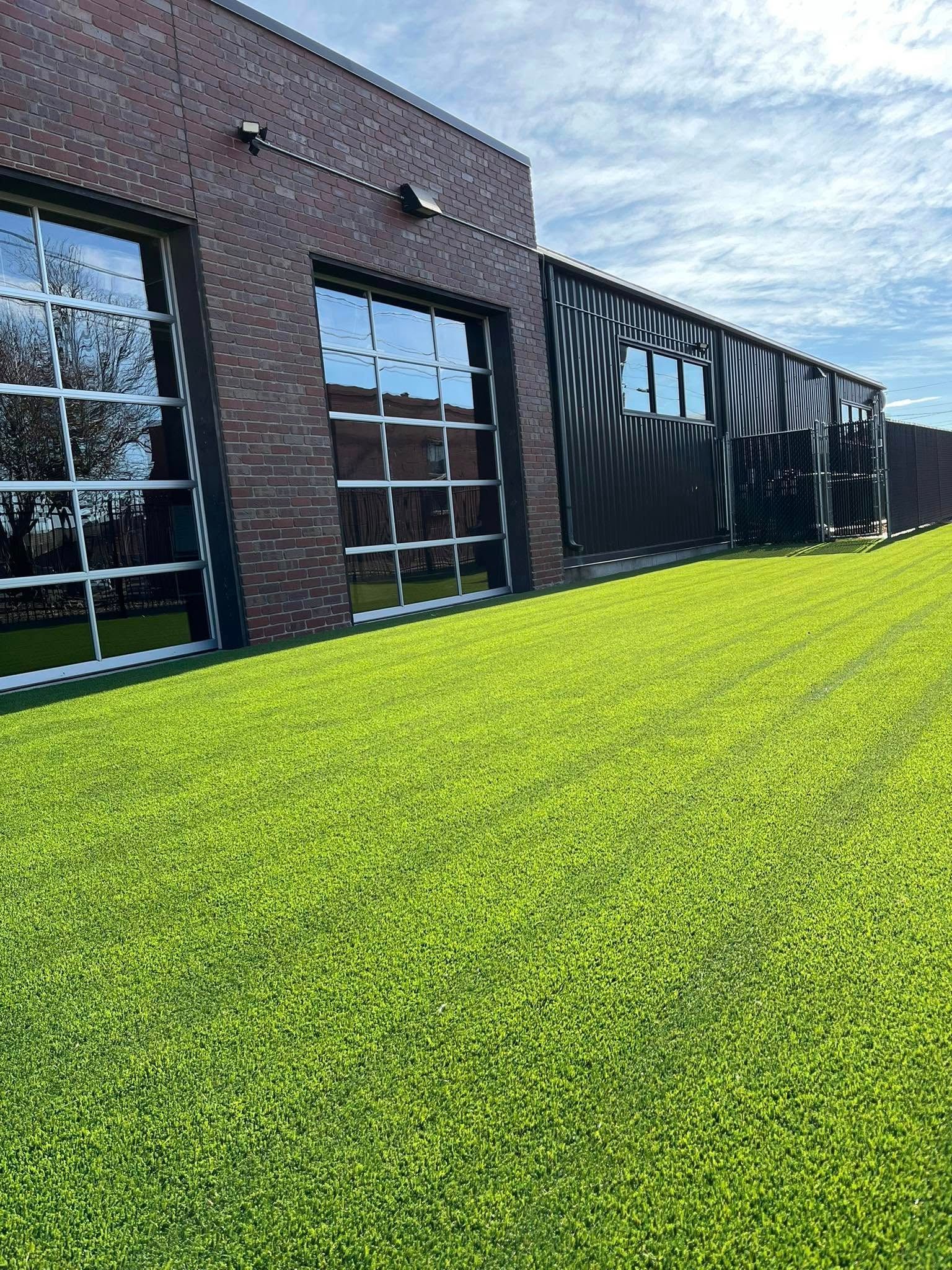 Brick building with large windows, adjacent to a field of vibrant green grass.
