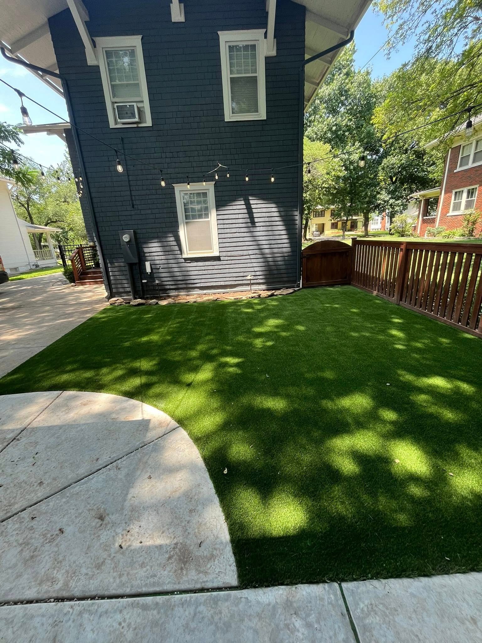 A backyard with a lush green lawn, a dark blue house, and a wooden fence.