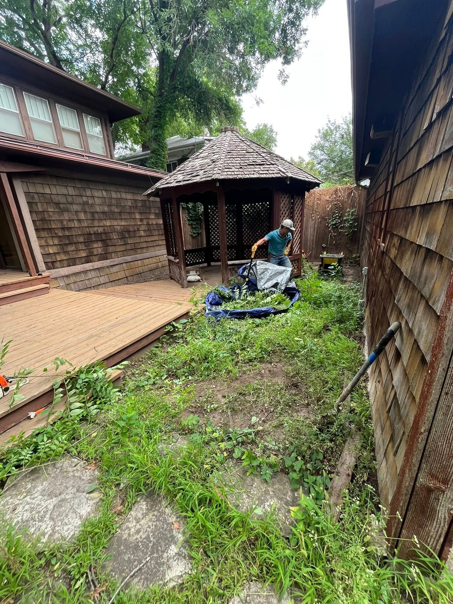 A person gardening near a gazebo and house with brown shingle siding.