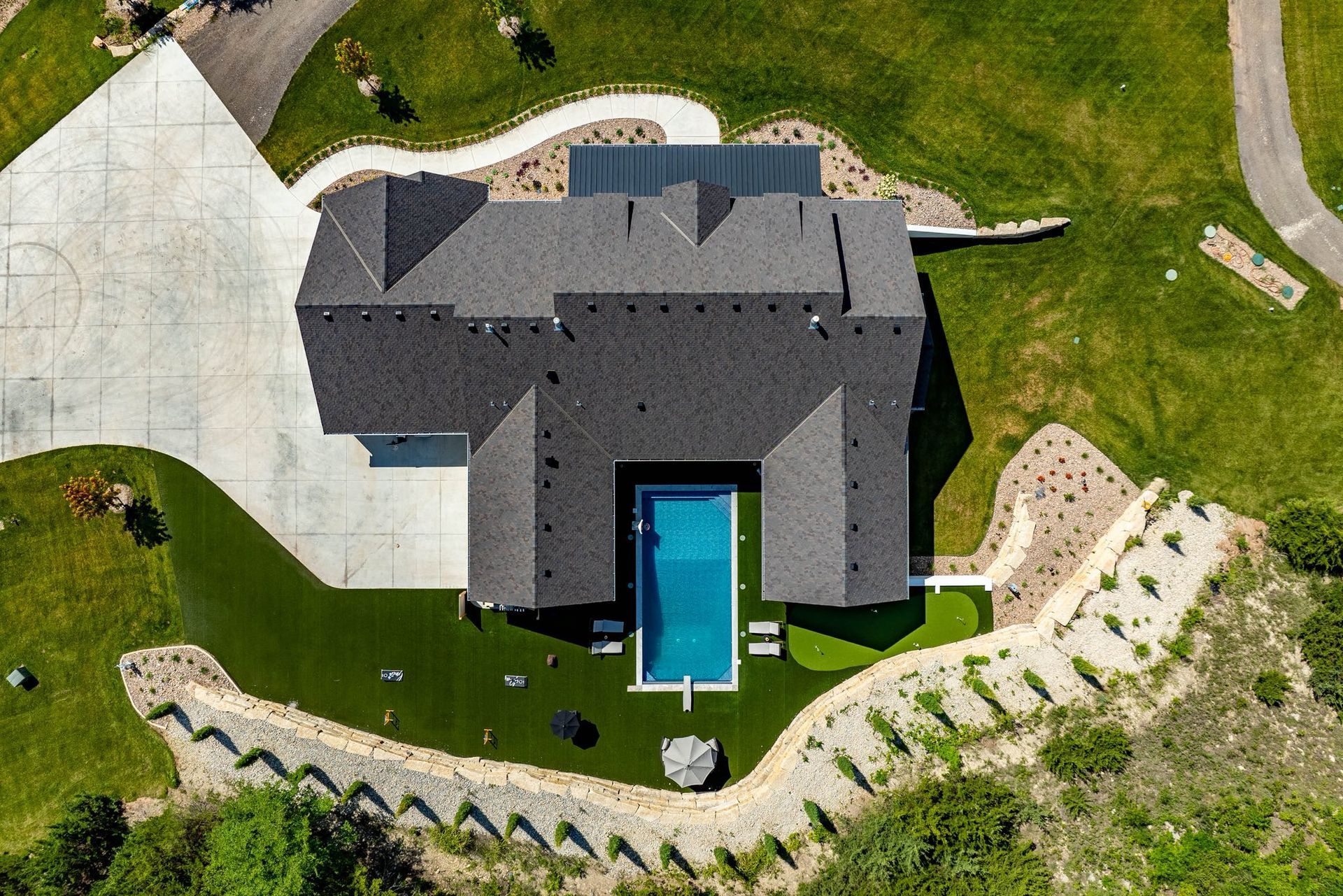 Aerial view of a modern home with a pool, surrounded by green grass and landscaping.