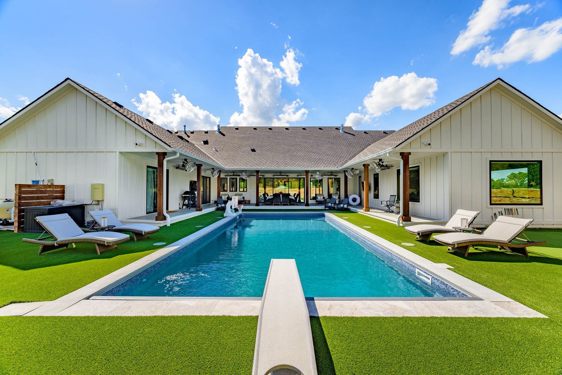 Backyard with rectangular pool, green lawn, white house, and blue sky.