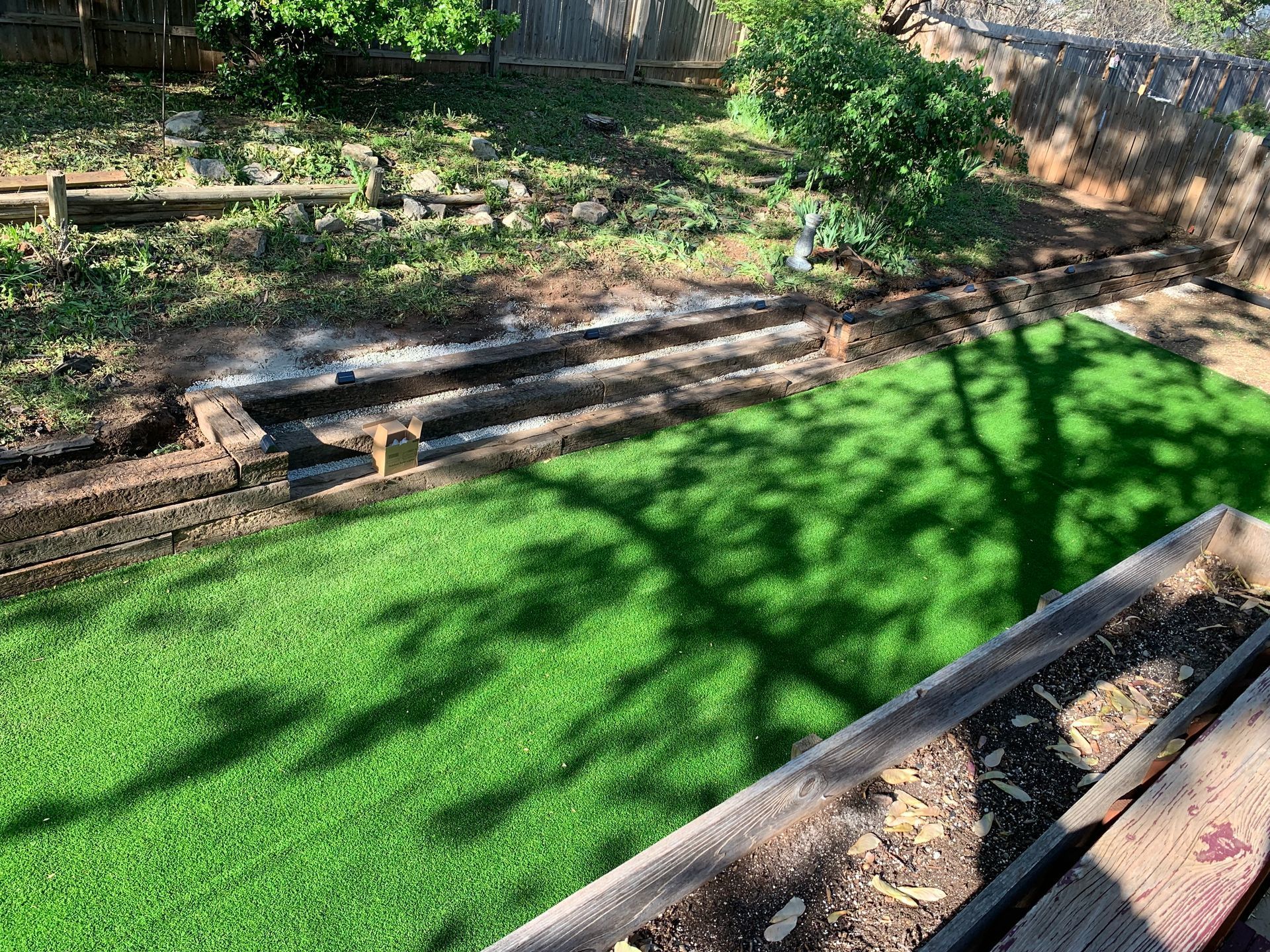Backyard with artificial turf, garden steps, and a raised bed in sunlight.