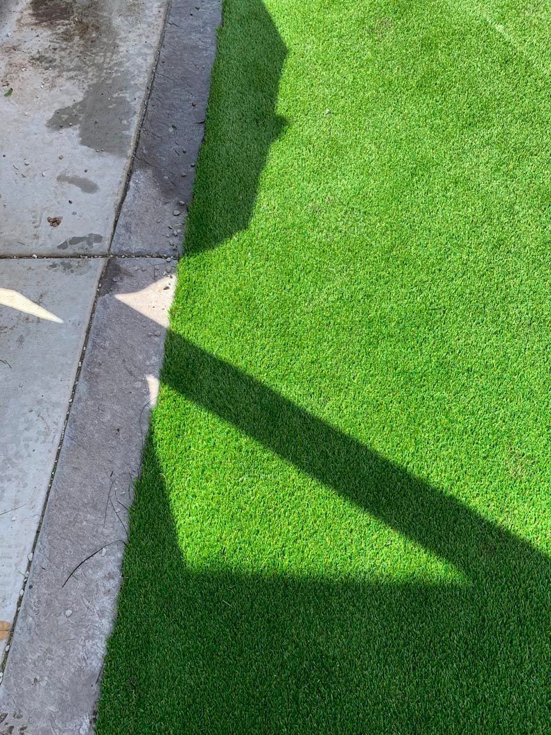 Green turf next to concrete with a shadow cast across it.