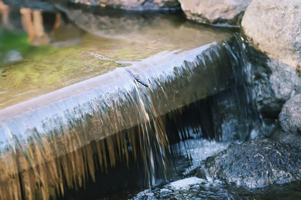 Waterfall cascading over a stone lip into a shallow pond.