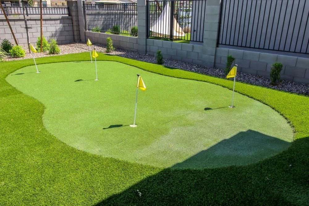 Backyard putting green with yellow flags, surrounded by a darker green lawn and decorative walls.