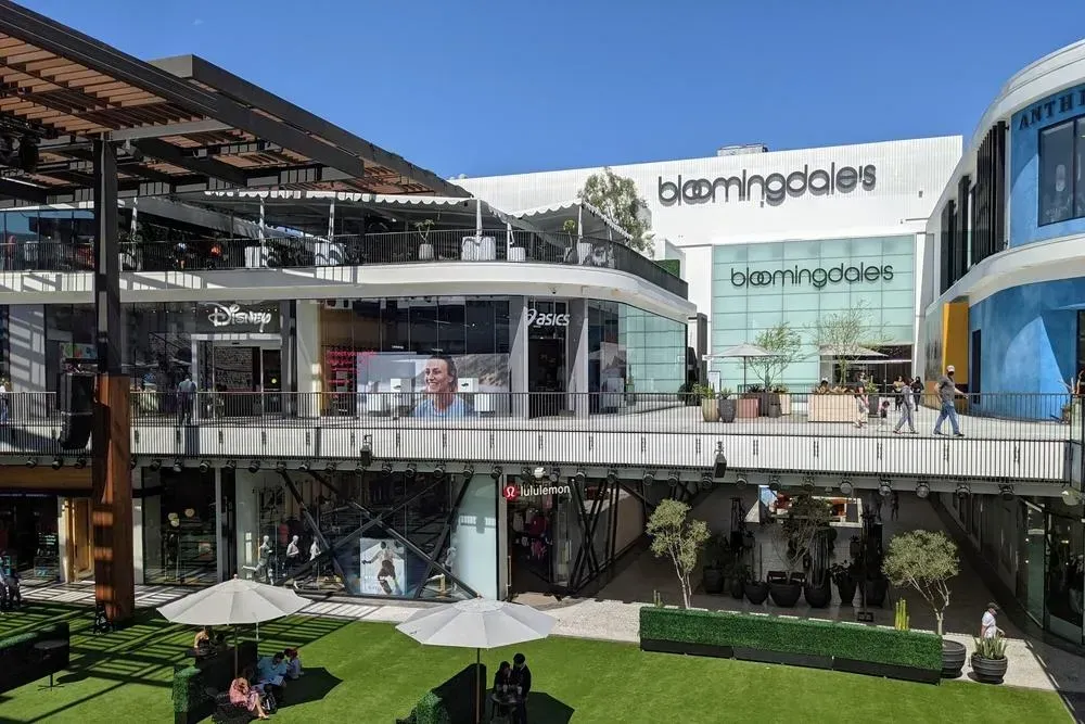 Multi-level outdoor mall with stores, Bloomingdale's in the background, blue sky.