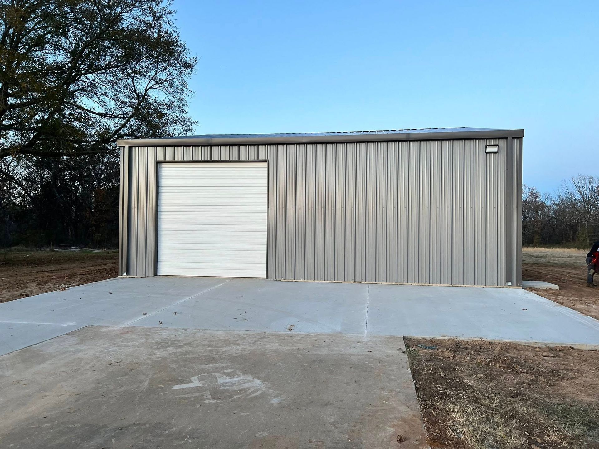 Metal storage building with a roll-up door, set on a concrete pad, against a blue sky.