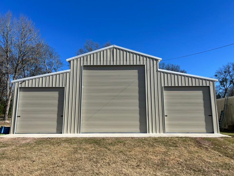 Tan metal barn with three garage doors on a bright, sunny day.