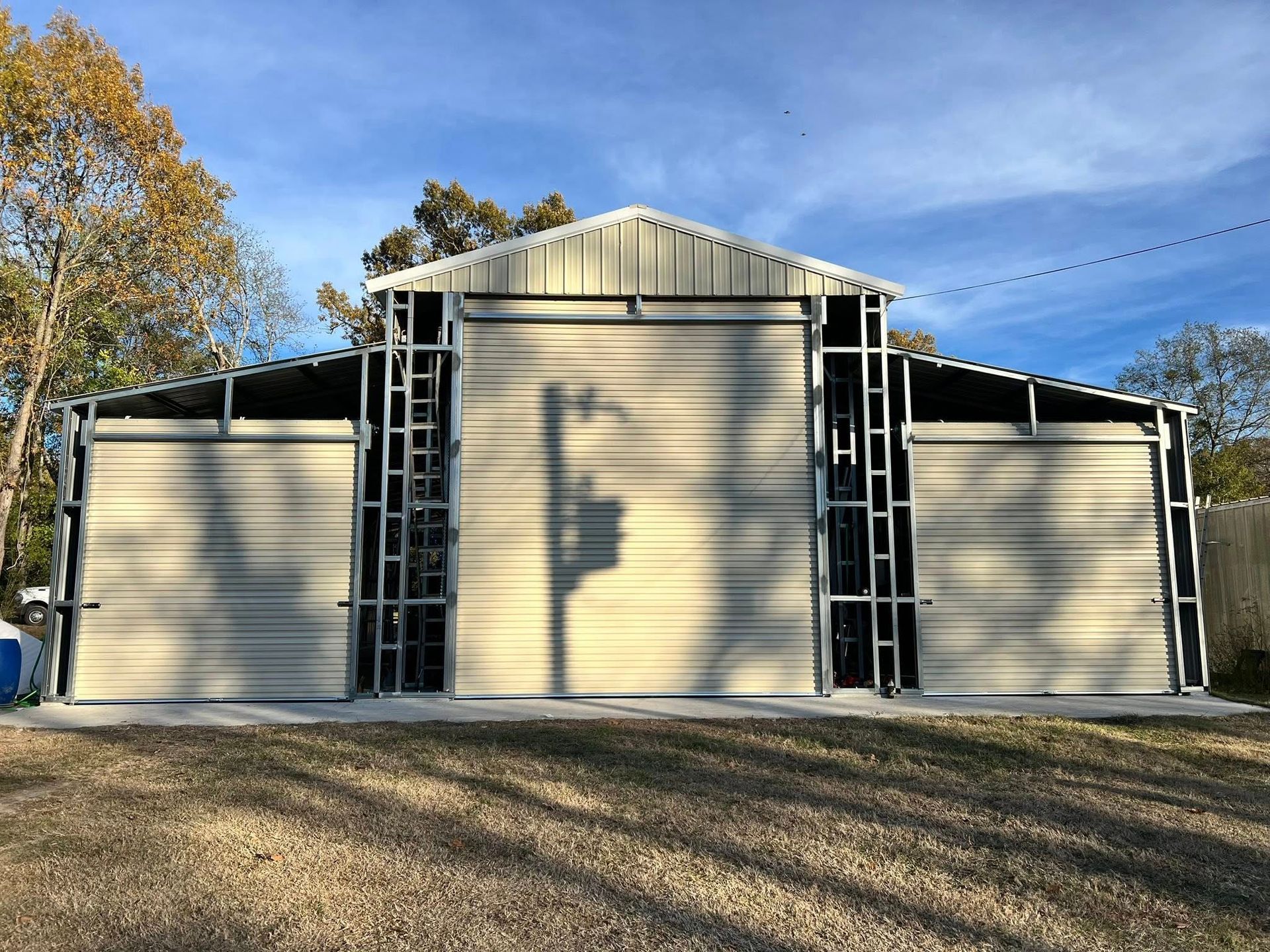 Tan metal barn structure with open steel framing, against a blue sky.