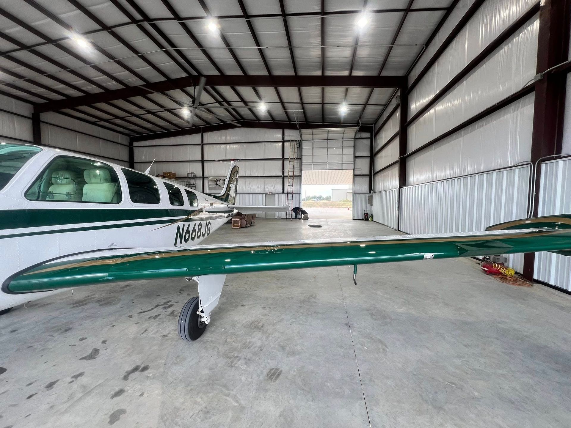 Airplane in a large hangar, white and green, with a man visible near the open door.