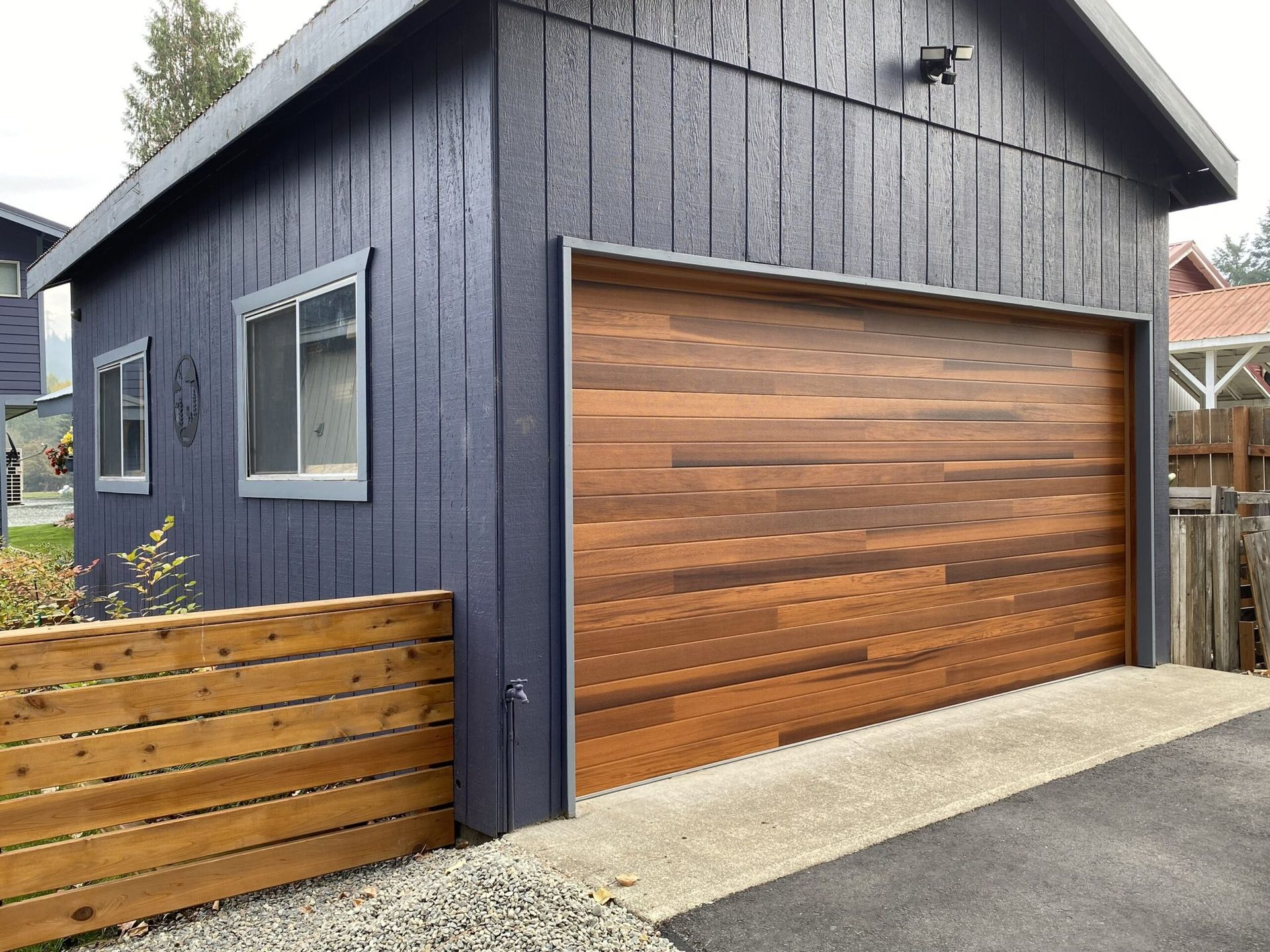 A dark blue garage with a wooden door, two windows, and a wooden fence.