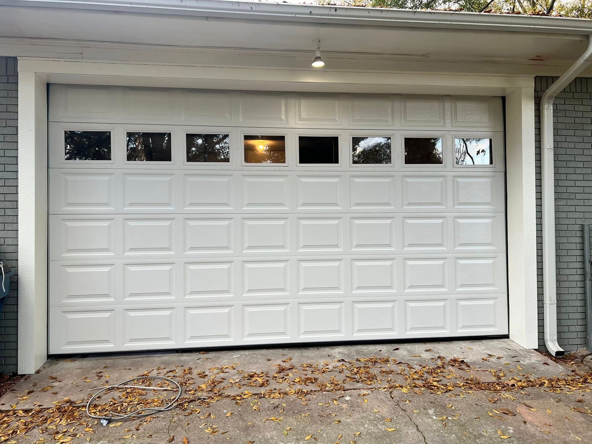 White garage door with windows, on a house, light above. Autumn leaves on the driveway.