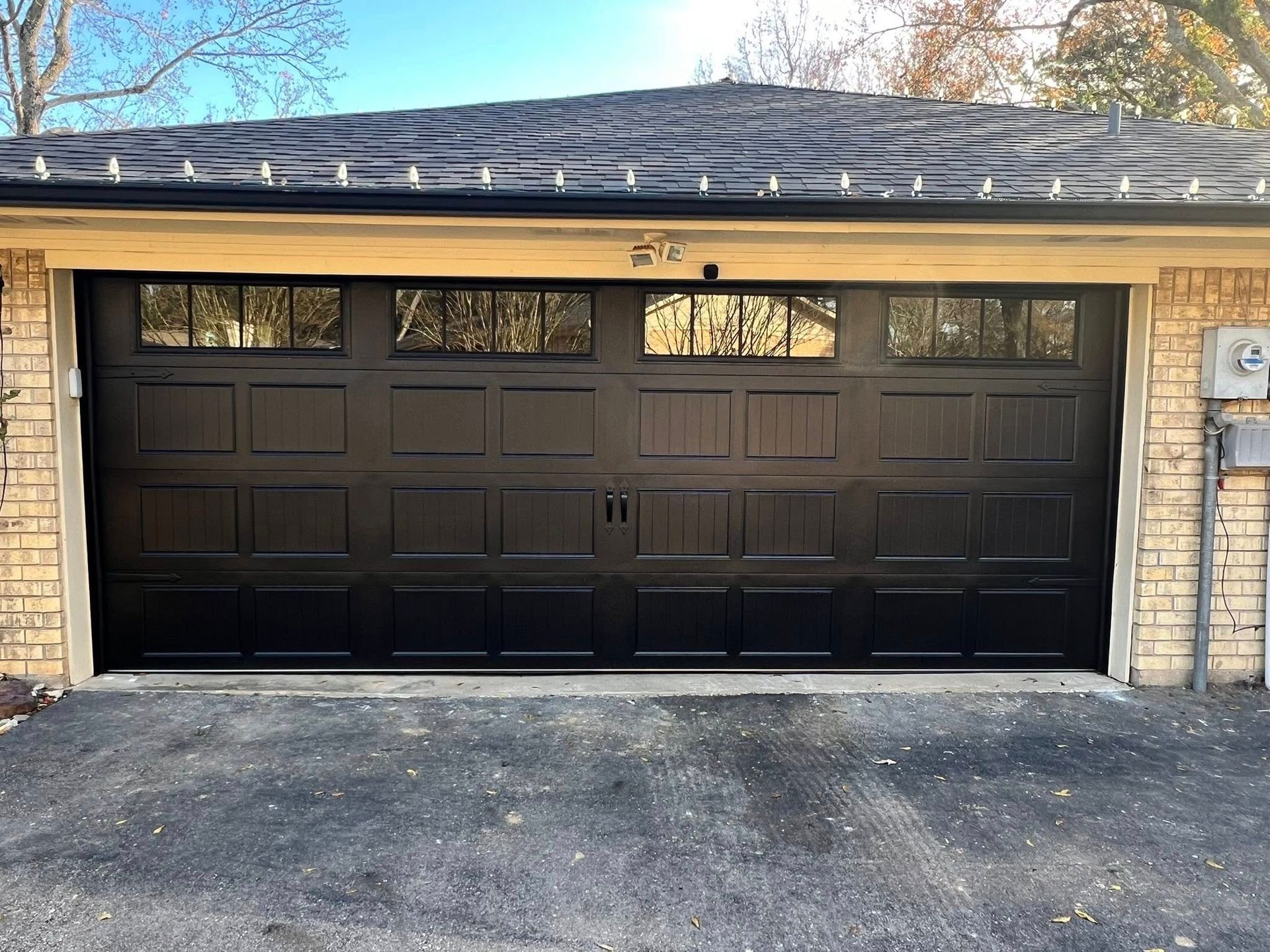 Black garage door with windows, set in brick building, asphalt driveway.