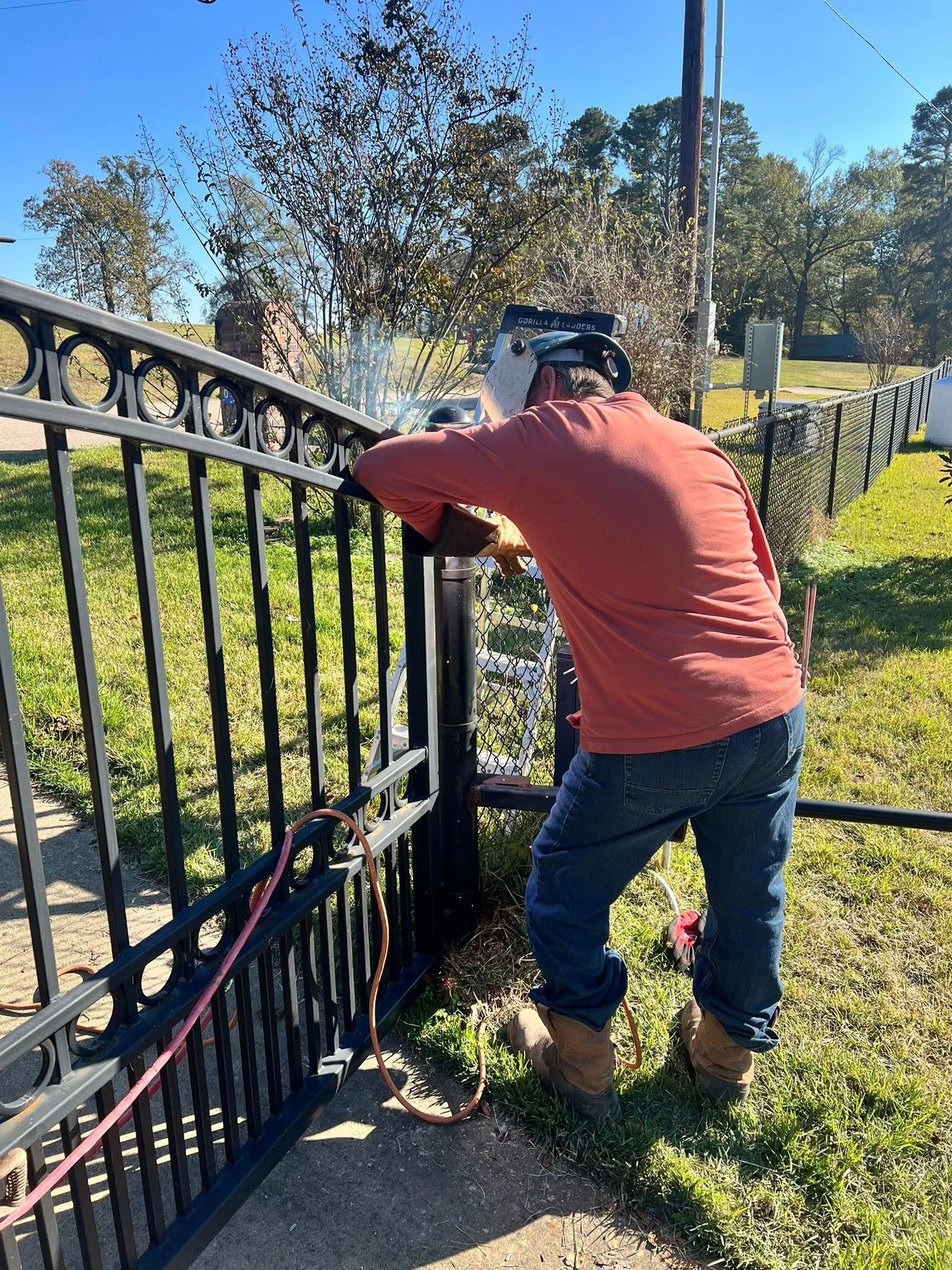 Person welding black metal fence outdoors on a sunny day.