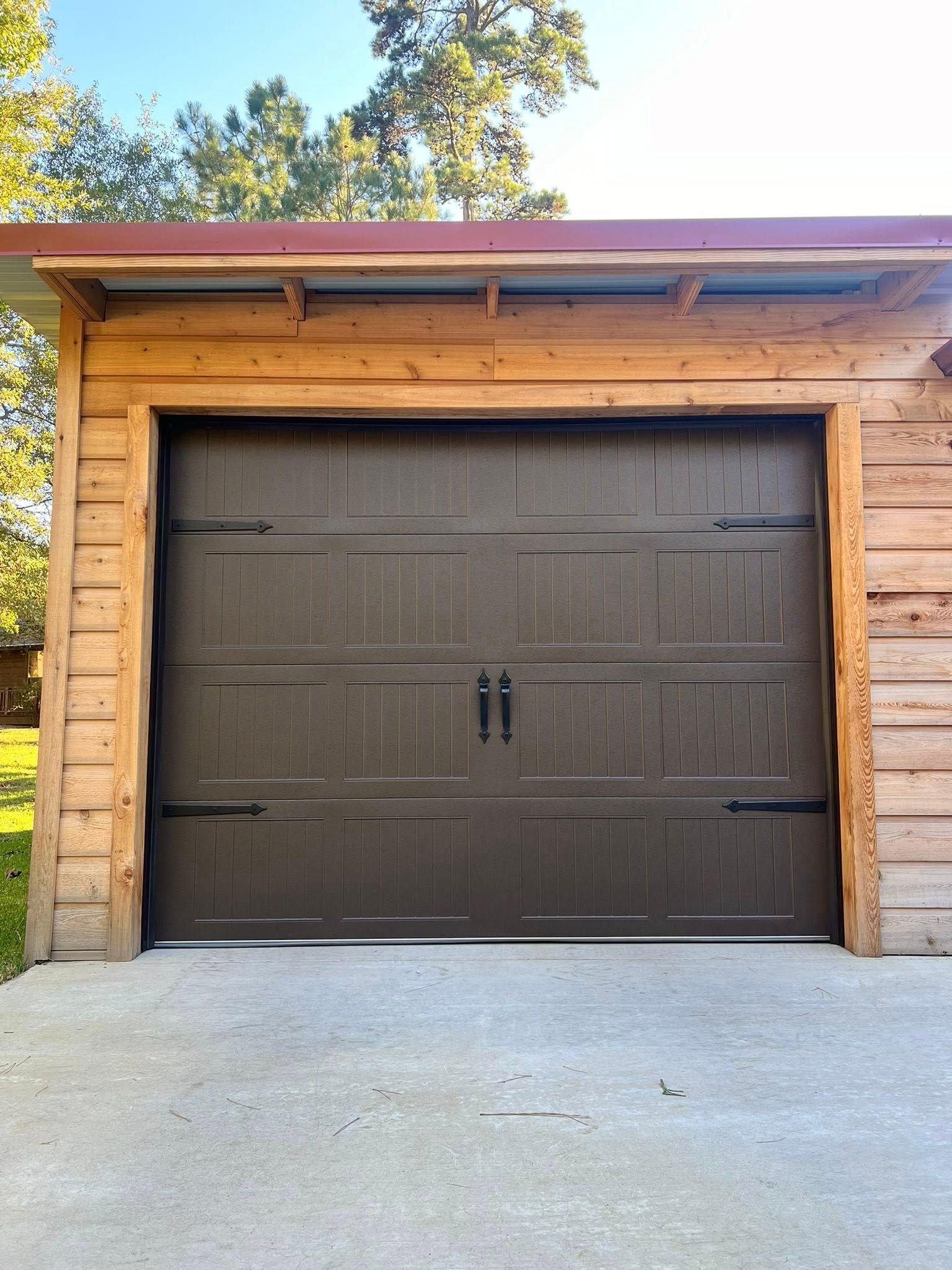 Brown garage door with dark handles, set in a wooden frame, and concrete driveway.