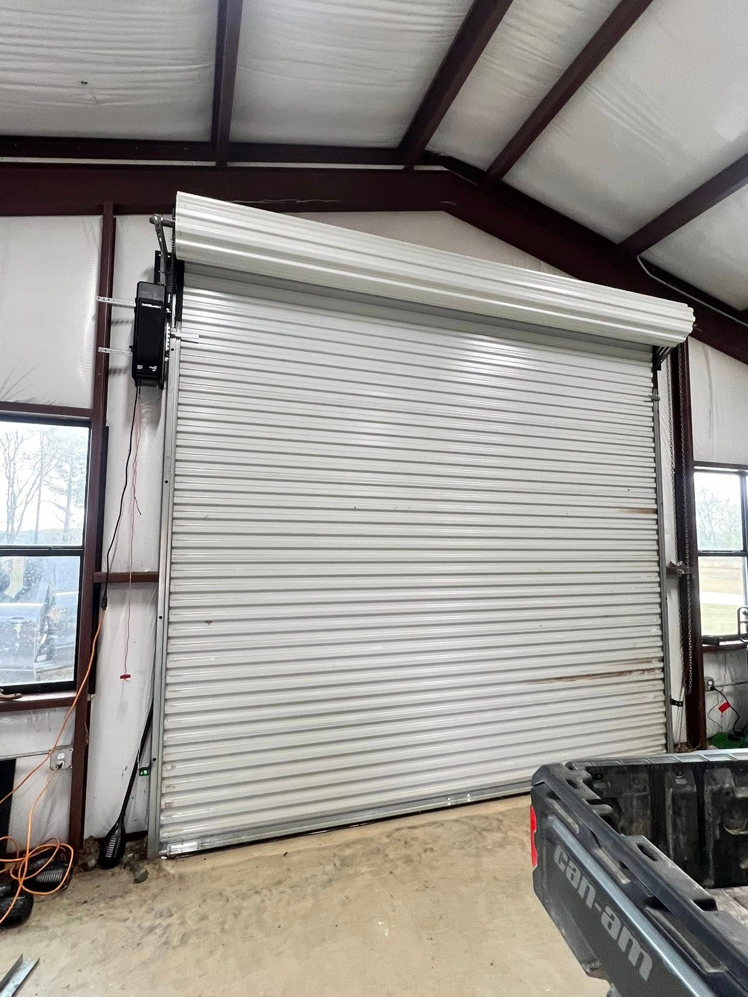 Metal roll-up garage door inside a building, partially open. The motor and frame are visible.