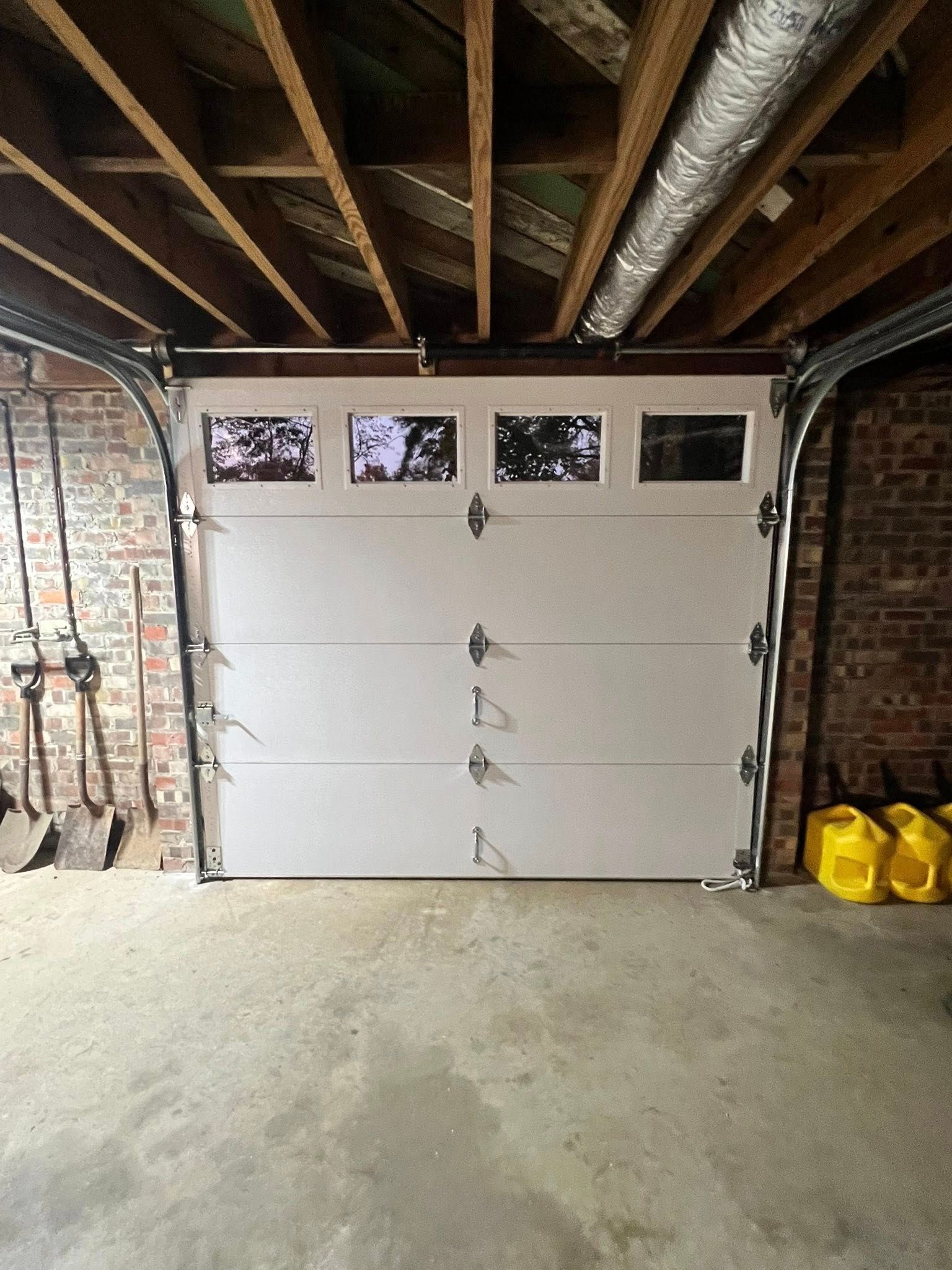 Closed white garage door with small windows. Inside a garage with exposed beams and brick walls.