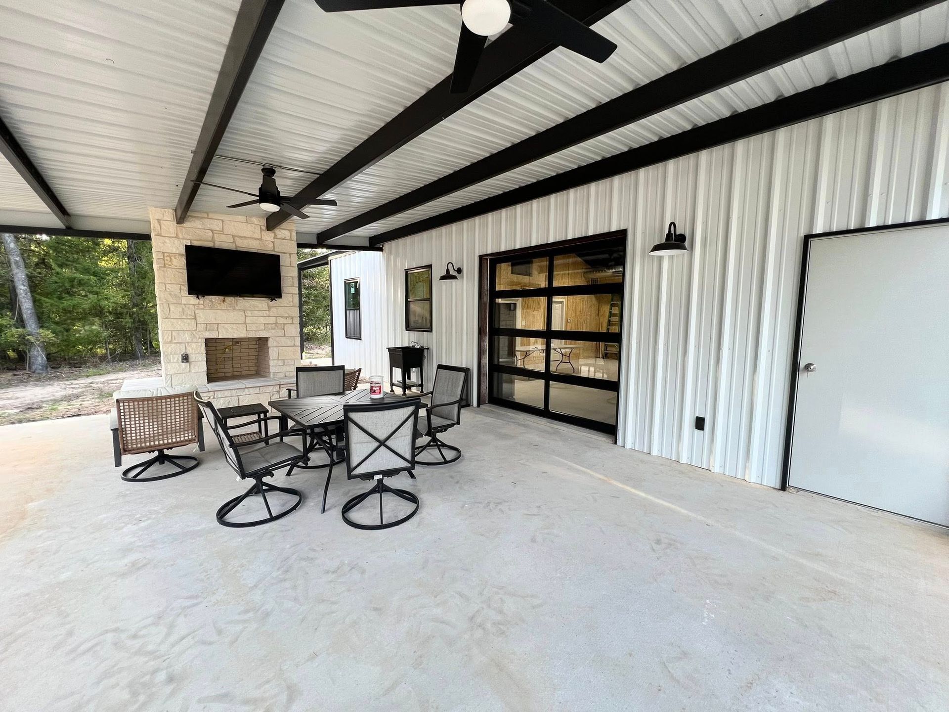 Patio with seating, fireplace, and mounted television under a white roof with black beams.