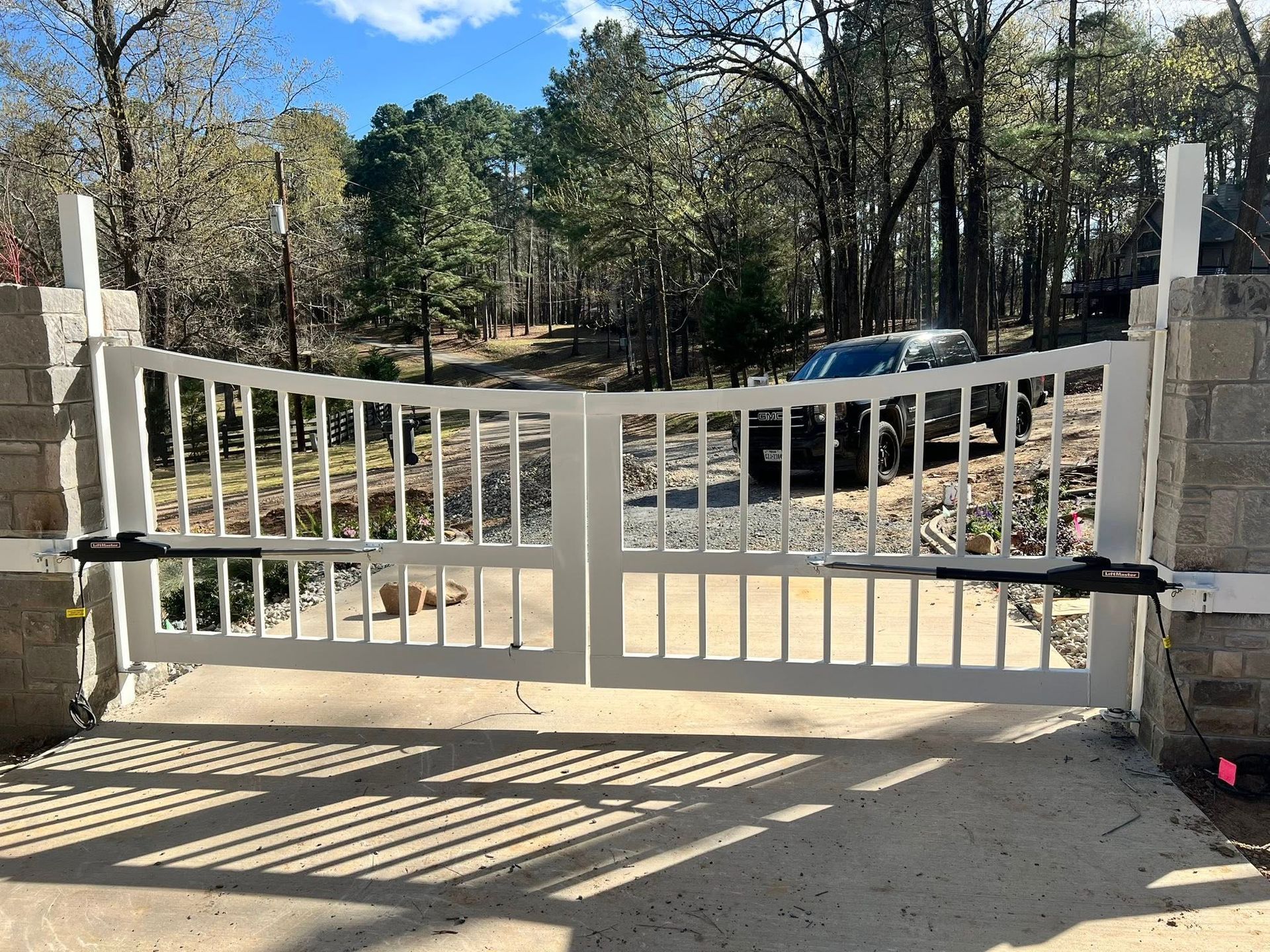 White automated gate, opening, set in concrete, with forest background.