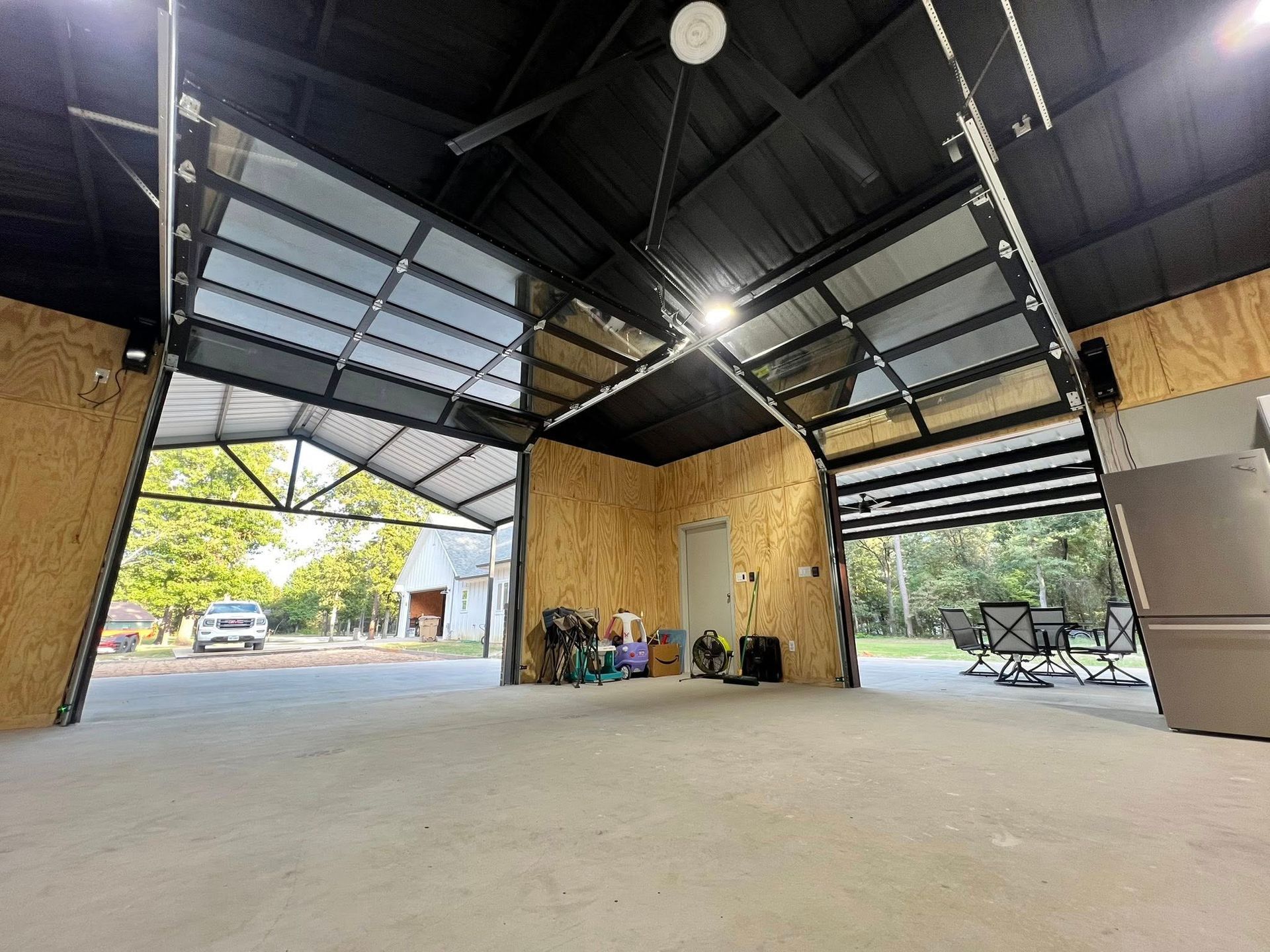 Interior view of a garage with open glass doors. The ceiling and doors are black, walls are unfinished wood.