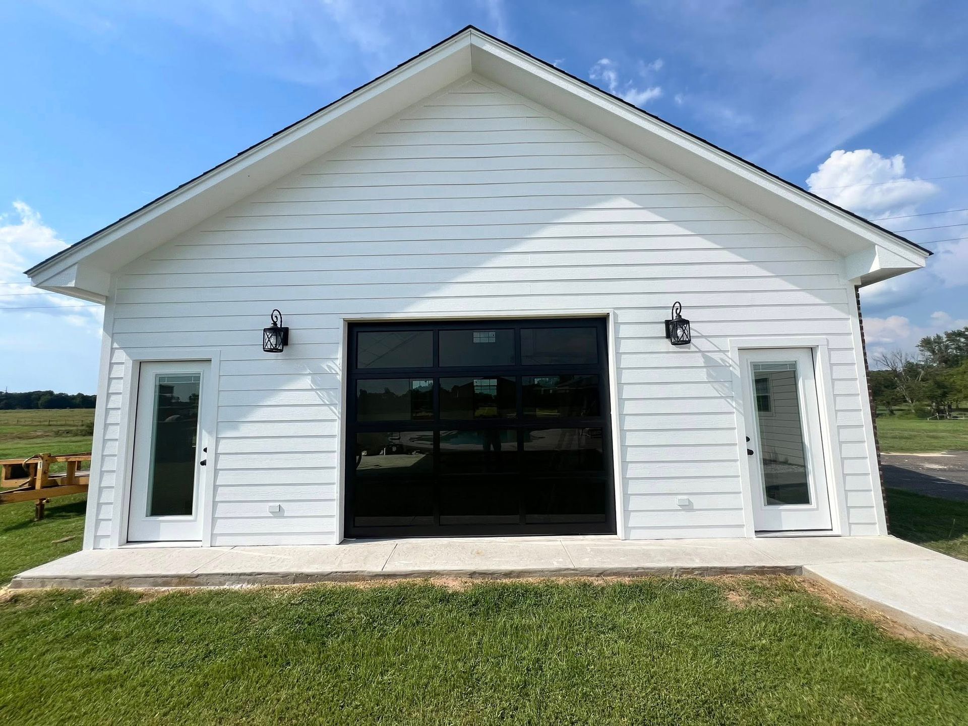 White building with a black glass garage door and two white doors. Black light fixtures. Sunny day.