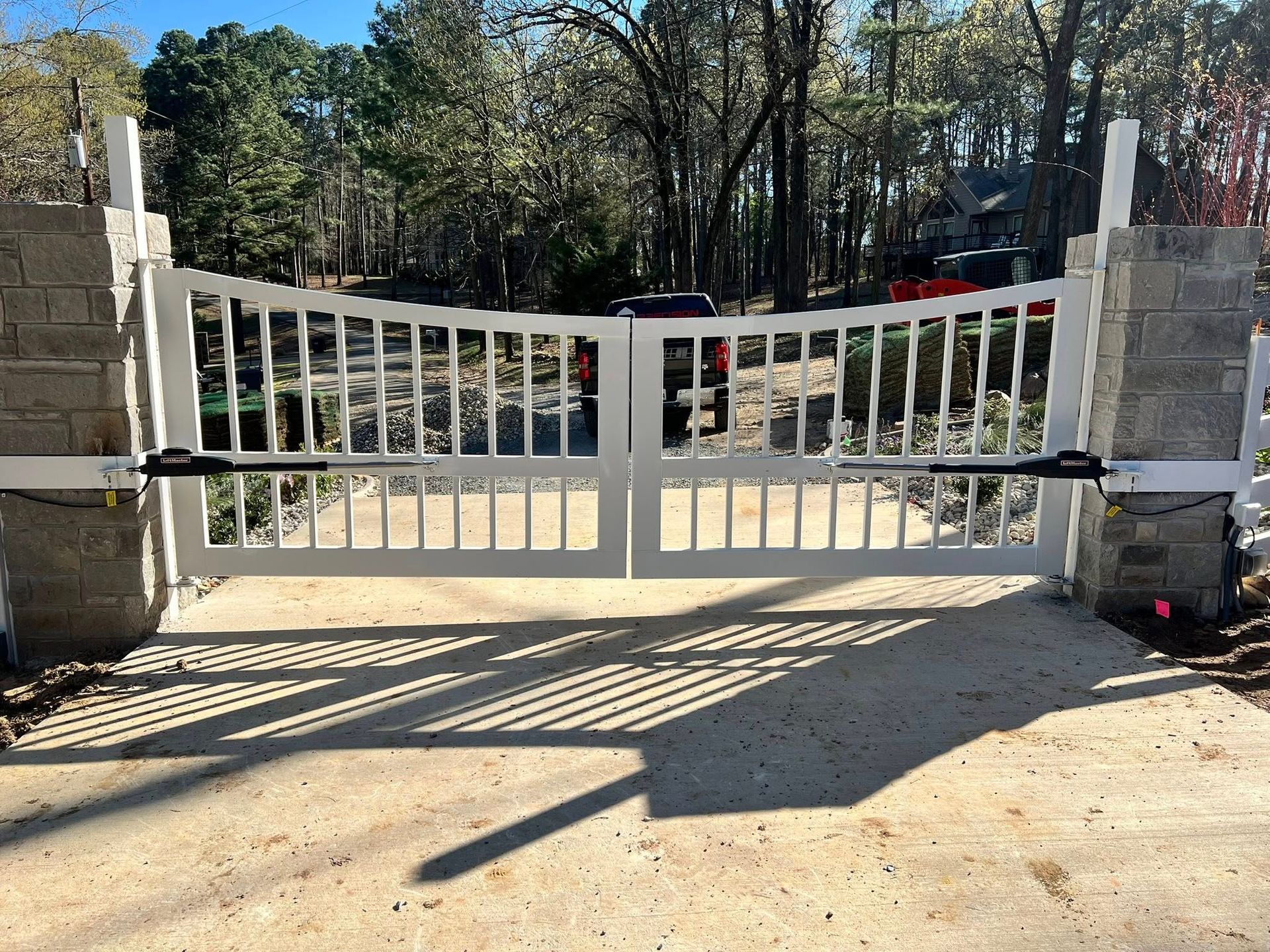 White, arched driveway gate with vertical bars, concrete posts, and automatic openers.