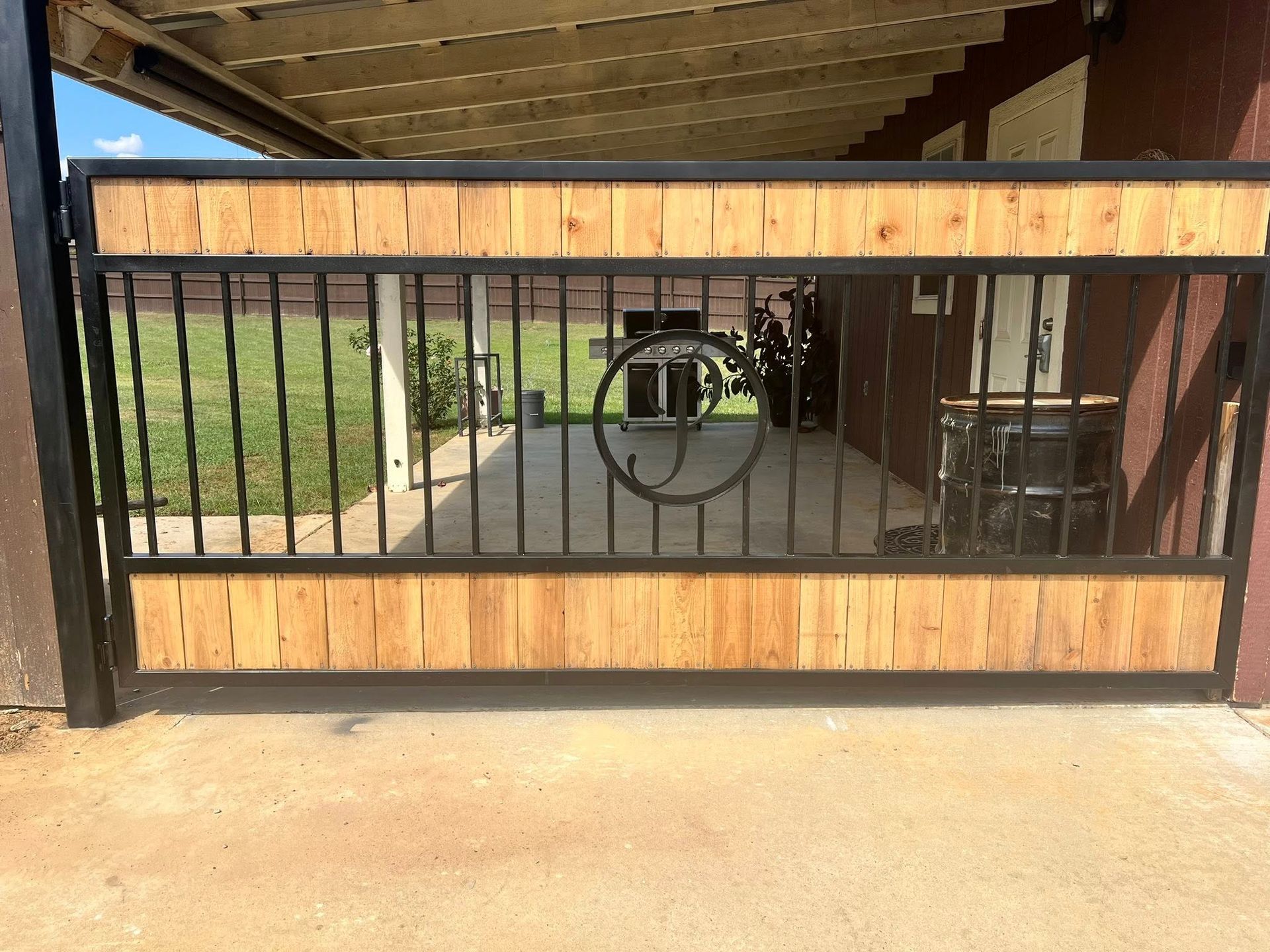 A wooden and metal gate with a circular design, spanning an outdoor walkway.