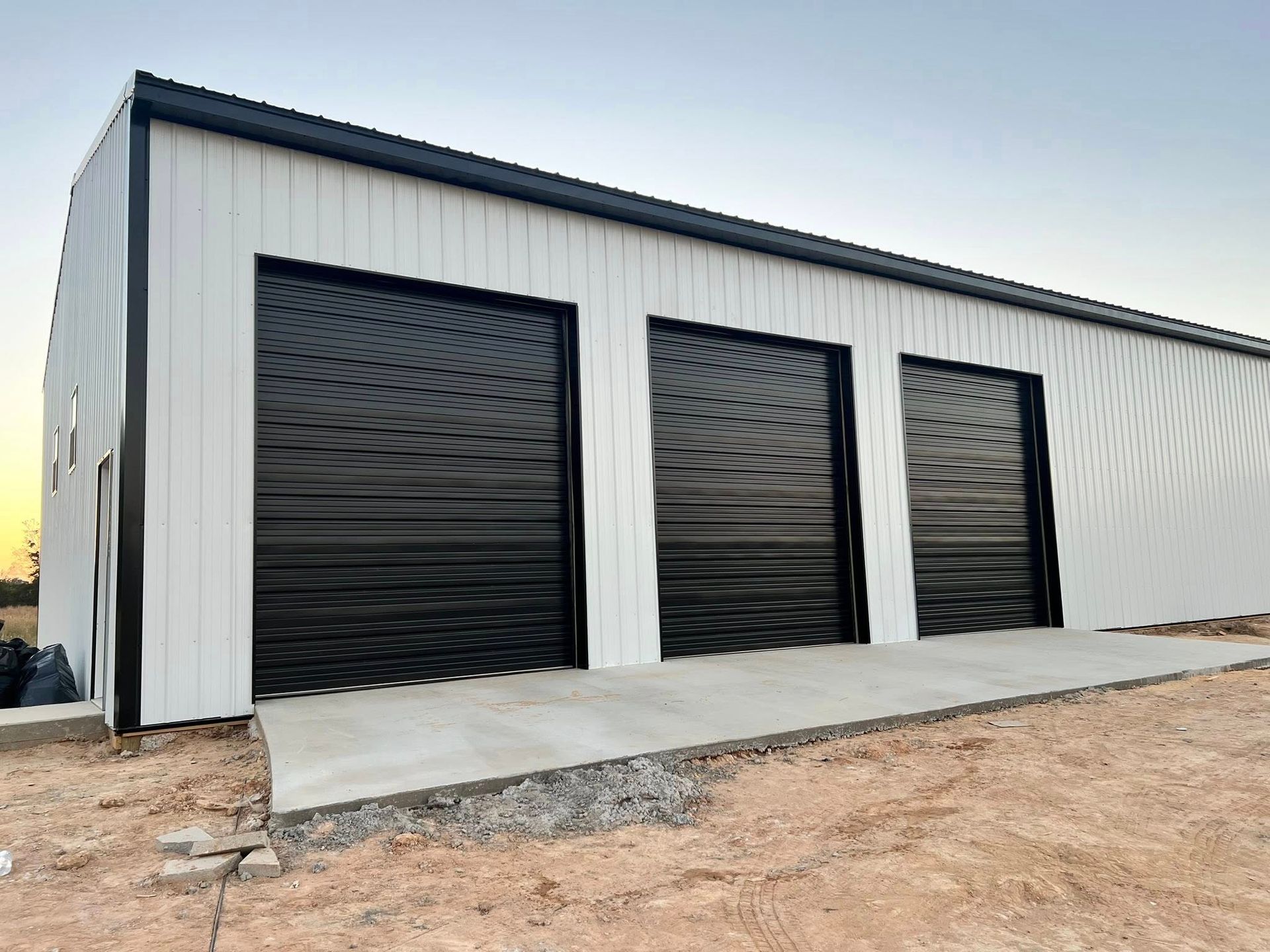 White metal building with three black garage doors, set against a blue sky.