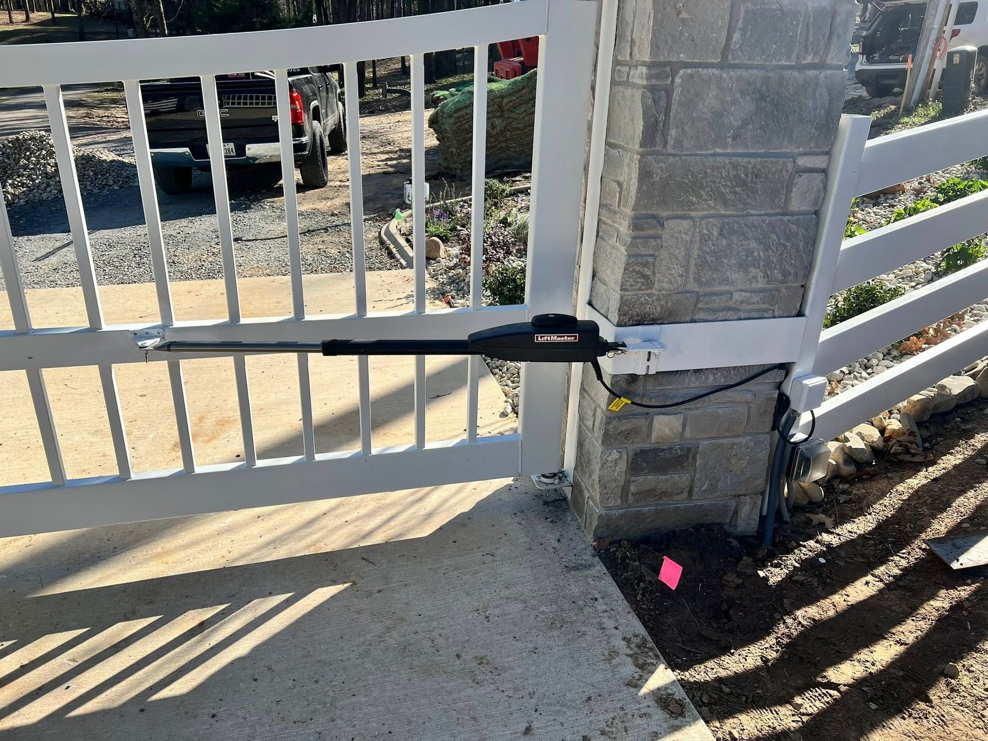 White gate with automated arm attached to a stone column. Black arm extends to open the gate.