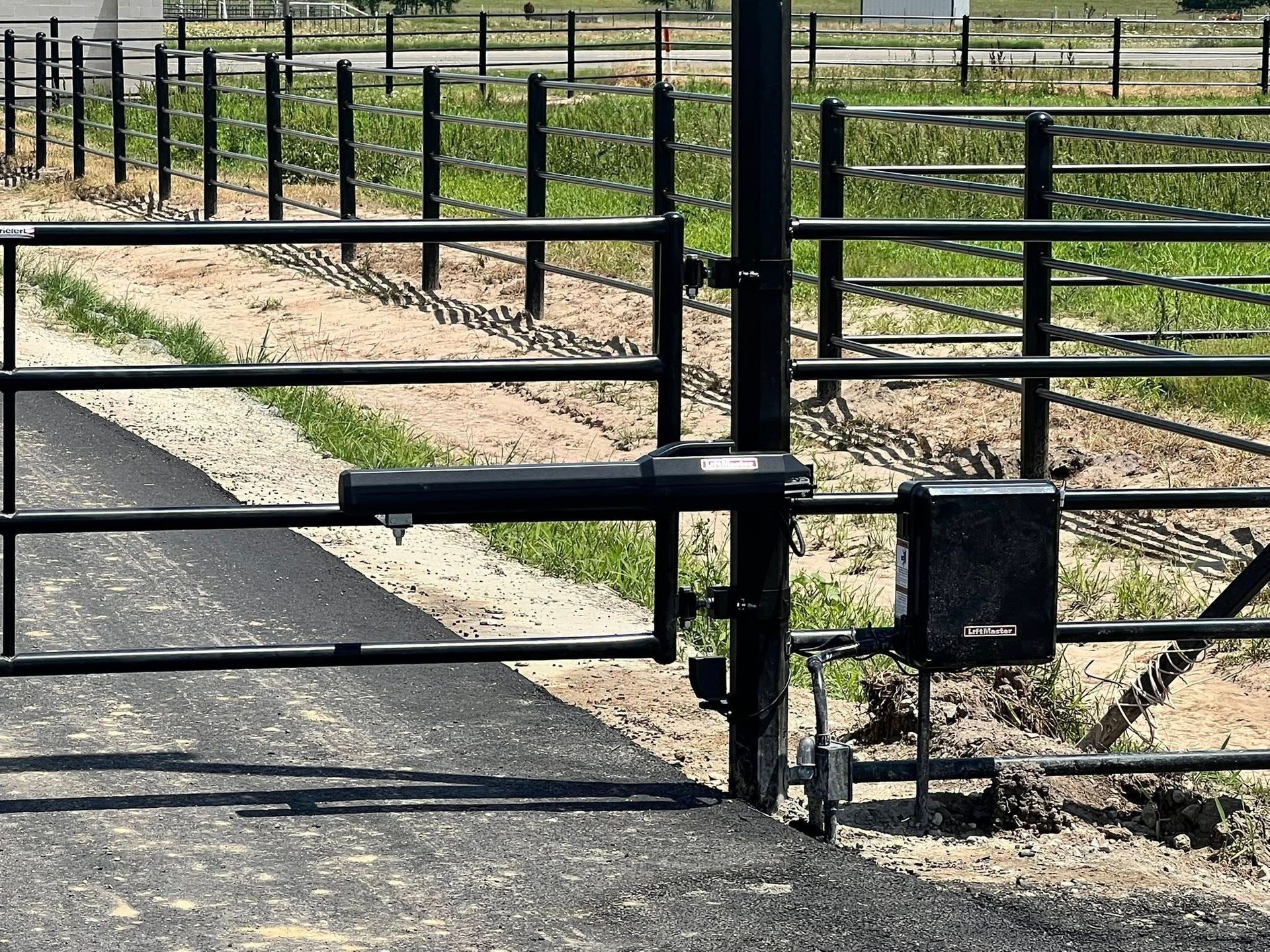 Black metal gate with automatic opener on a paved driveway.