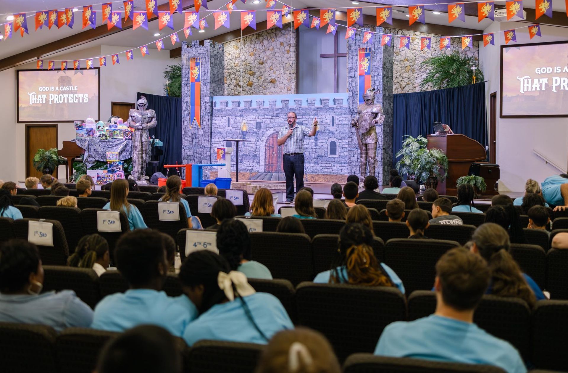 A man speaks to a crowd in a church decorated for a medieval-themed event.