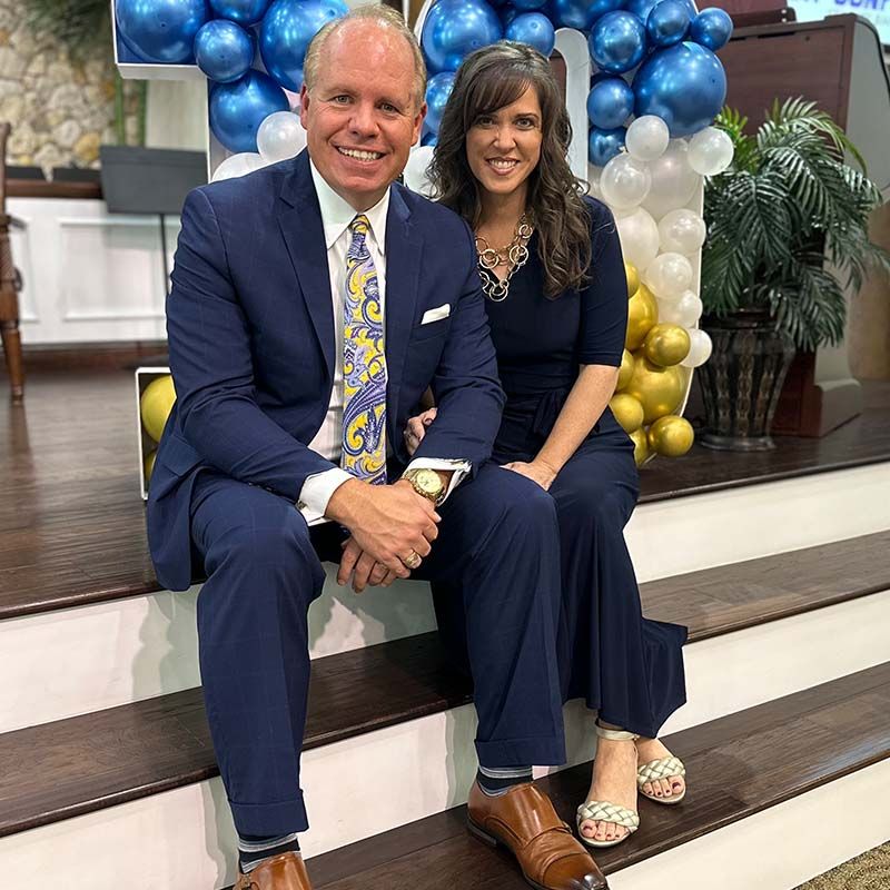 Pastor and Mrs. Glenn Wiggins seated on carpeted stairs.