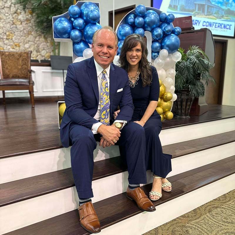 Pastor and Mrs. Glenn Wiggins seated on carpeted stairs.
