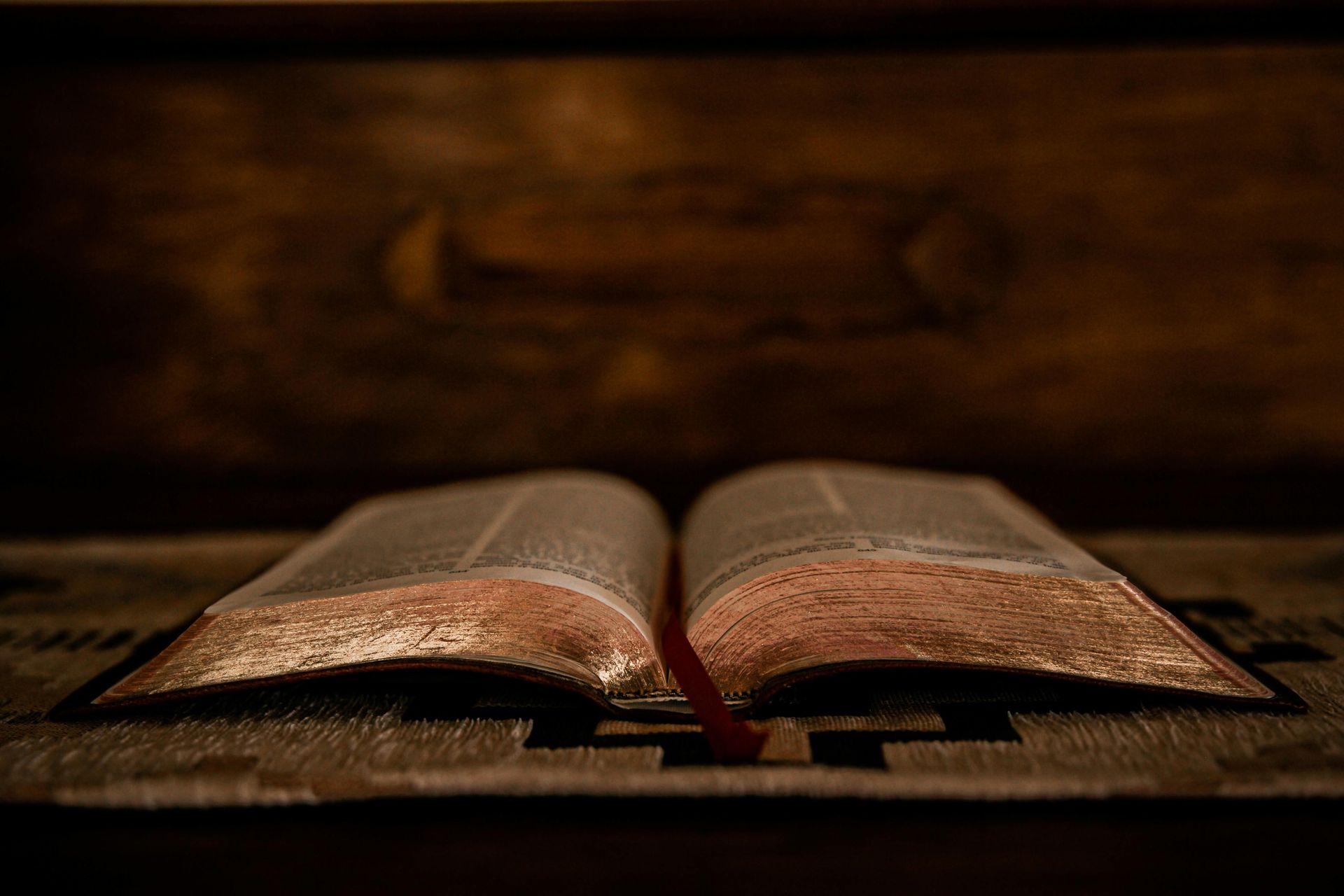 Open antique book on a wooden surface; red ribbon bookmark; warm lighting; dark background.