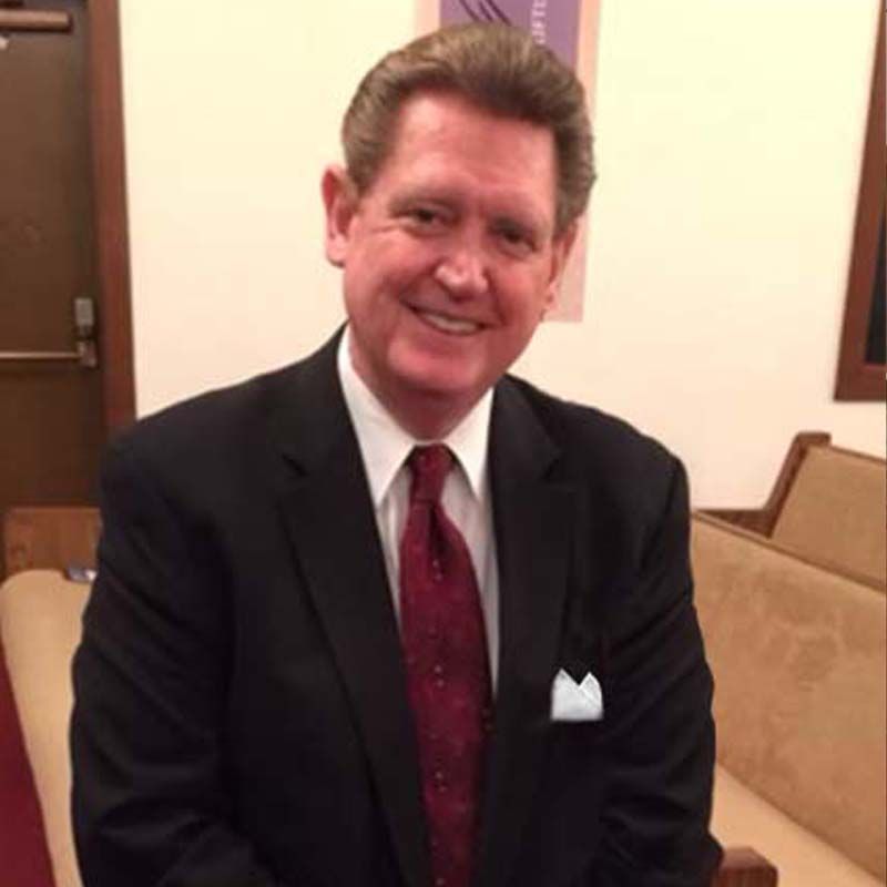 Man in suit, smiling, red tie, white pocket square, seated in a church.