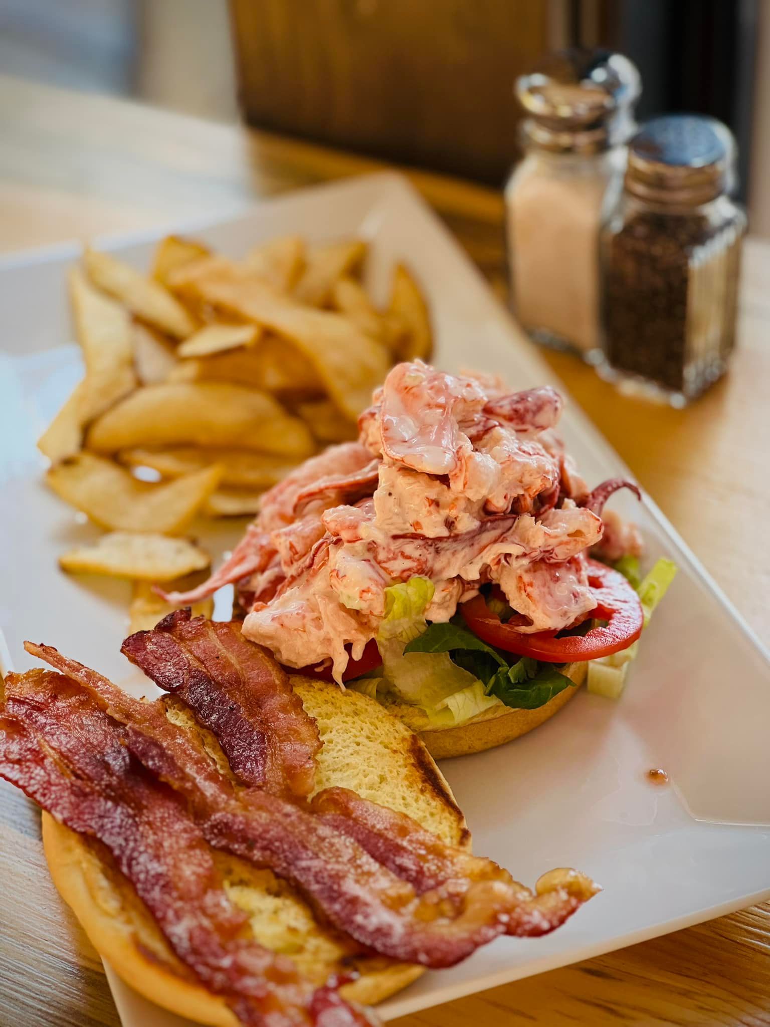 A sandwich with bacon and french fries on a plate on a table.