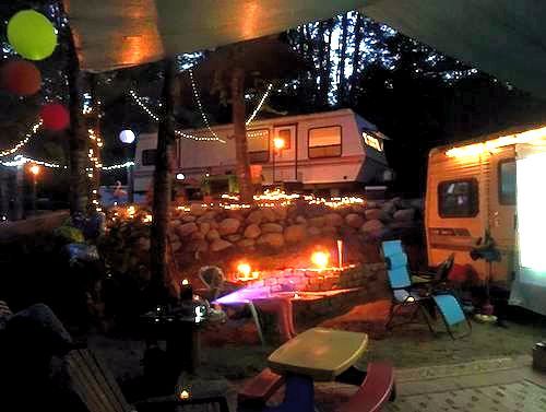 A rv is parked next to a picnic table and chairs at night.