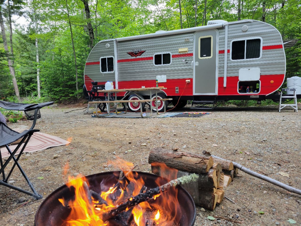 A red and silver trailer is parked next to a fire pit.
